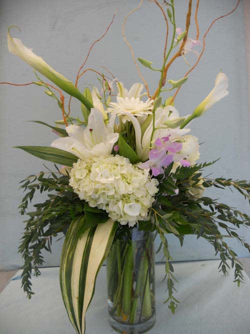 Tall white floral arrangement in a glass vase with orchids and lilies