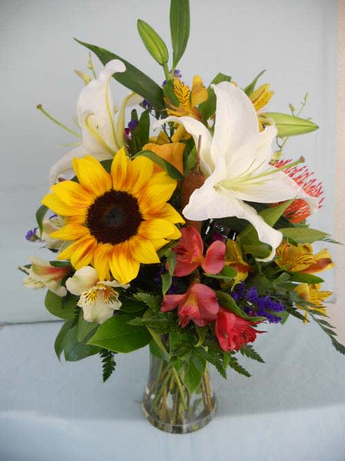 Mixed bouquet with sunflowers, white lilies, and colorful blooms in a glass vase