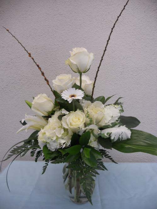 White roses and lilies arranged in a glass vase with a daisy accent