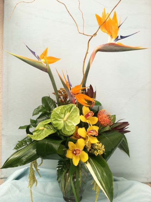 Tropical flower arrangement with orange bird-of-paradise and yellow orchids in a glass vase