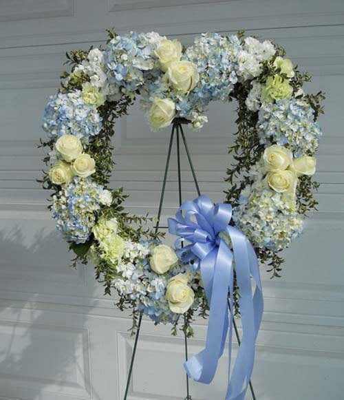 Heart-shaped floral wreath with pale blue and white flowers and a blue ribbon