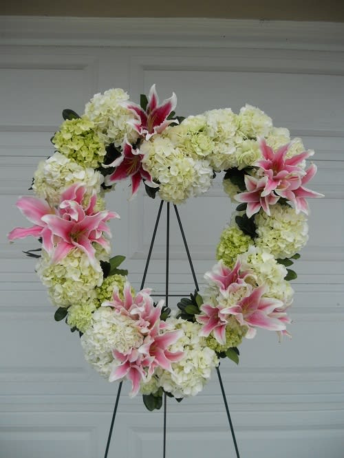 Heart-shaped floral wreath with pink lilies and white hydrangeas on a stand