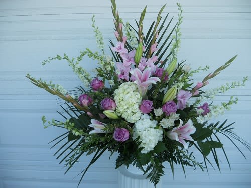 Tall floral arrangement with pink lilies, purple roses, and white hydrangeas in a white vase.