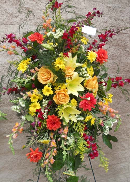 Tall standing spray of mixed flowers in yellow, orange, red, and white