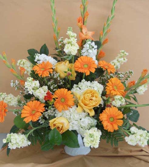 Orange gerbera daisies and yellow roses in a white vase