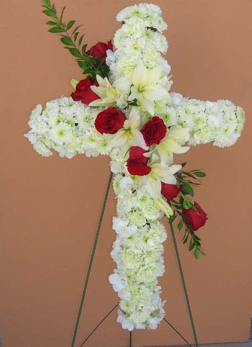 Cross-shaped floral tribute with white flowers and red roses on a stand
