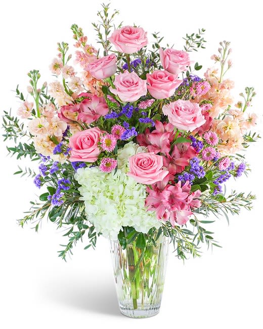 Pink roses and mixed flowers arranged in a clear glass vase