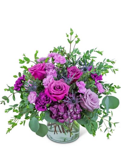 Purple roses and carnations in a glass vase with greenery