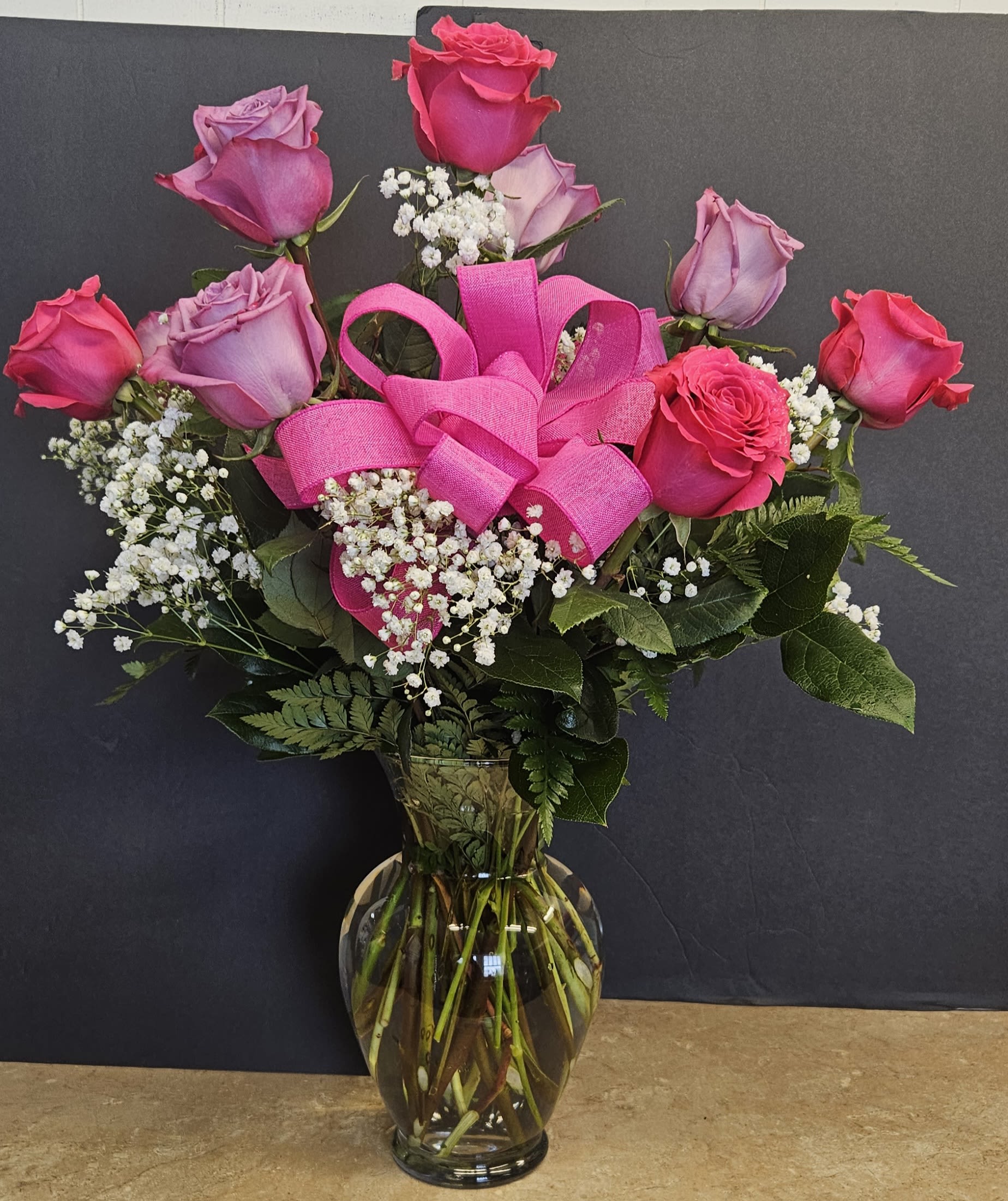 Pink and lavender roses in a glass vase with a bright pink ribbon