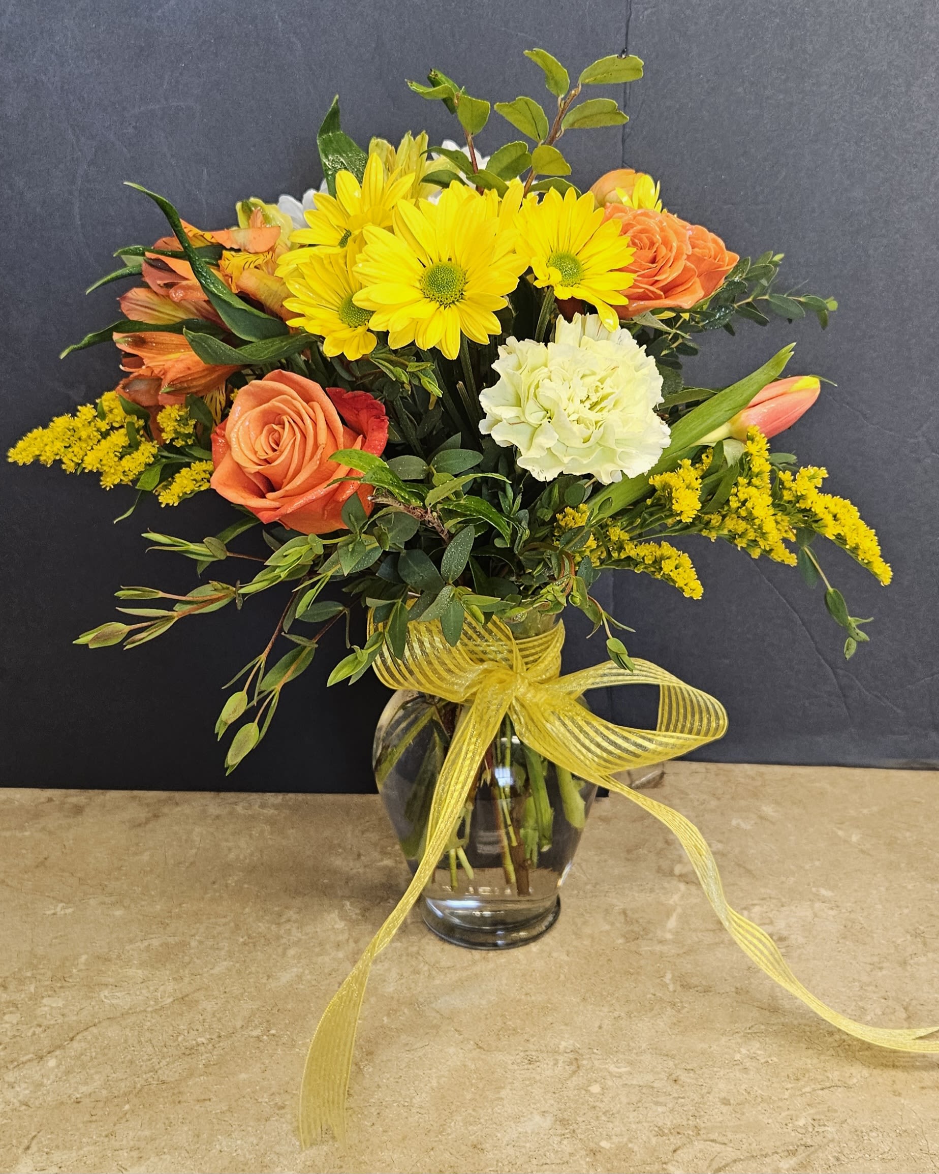 Bouquet of yellow daisies, orange roses, and white carnations in a glass vase
