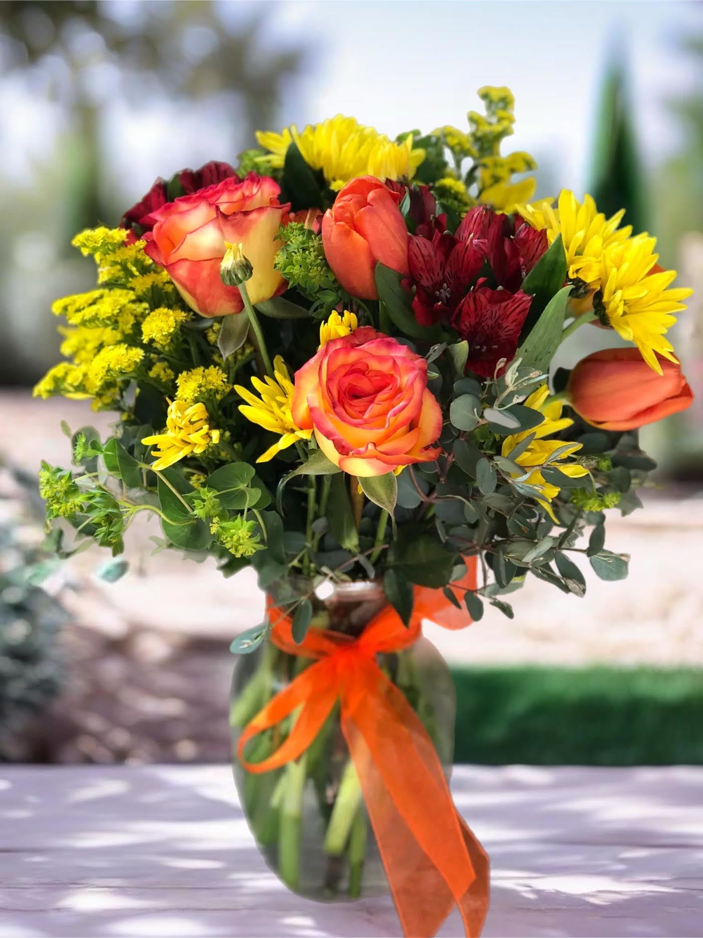 Bouquet of orange roses and yellow daisies in a glass vase with an orange ribbon