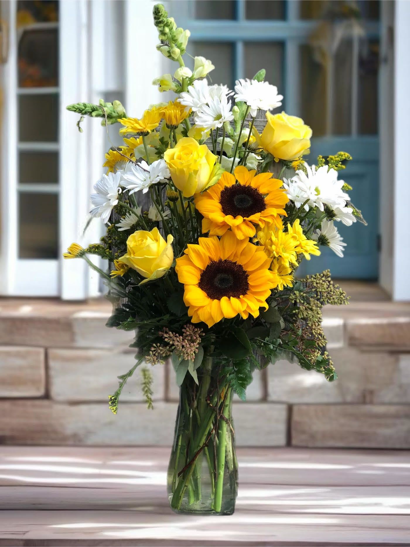 Yellow roses and sunflowers in a clear glass vase with white daisies