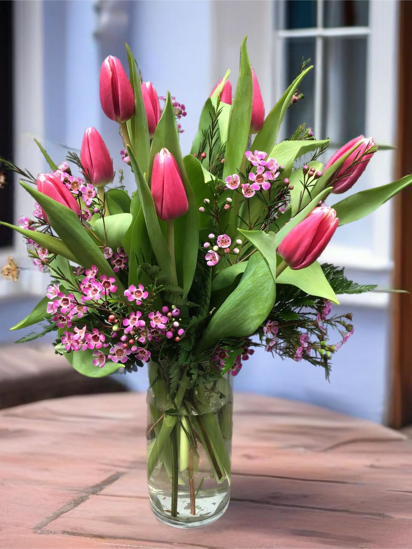 Pink tulips arranged in a clear glass vase with small pink blossoms