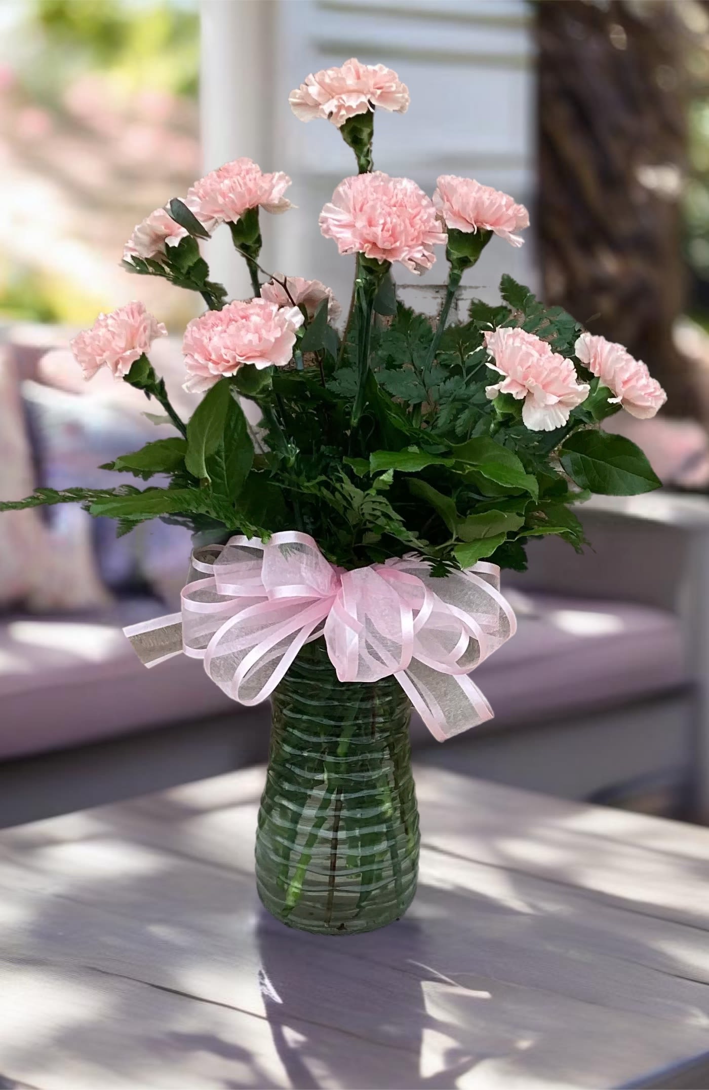 Pink carnations in a green glass vase with a pink ribbon bow