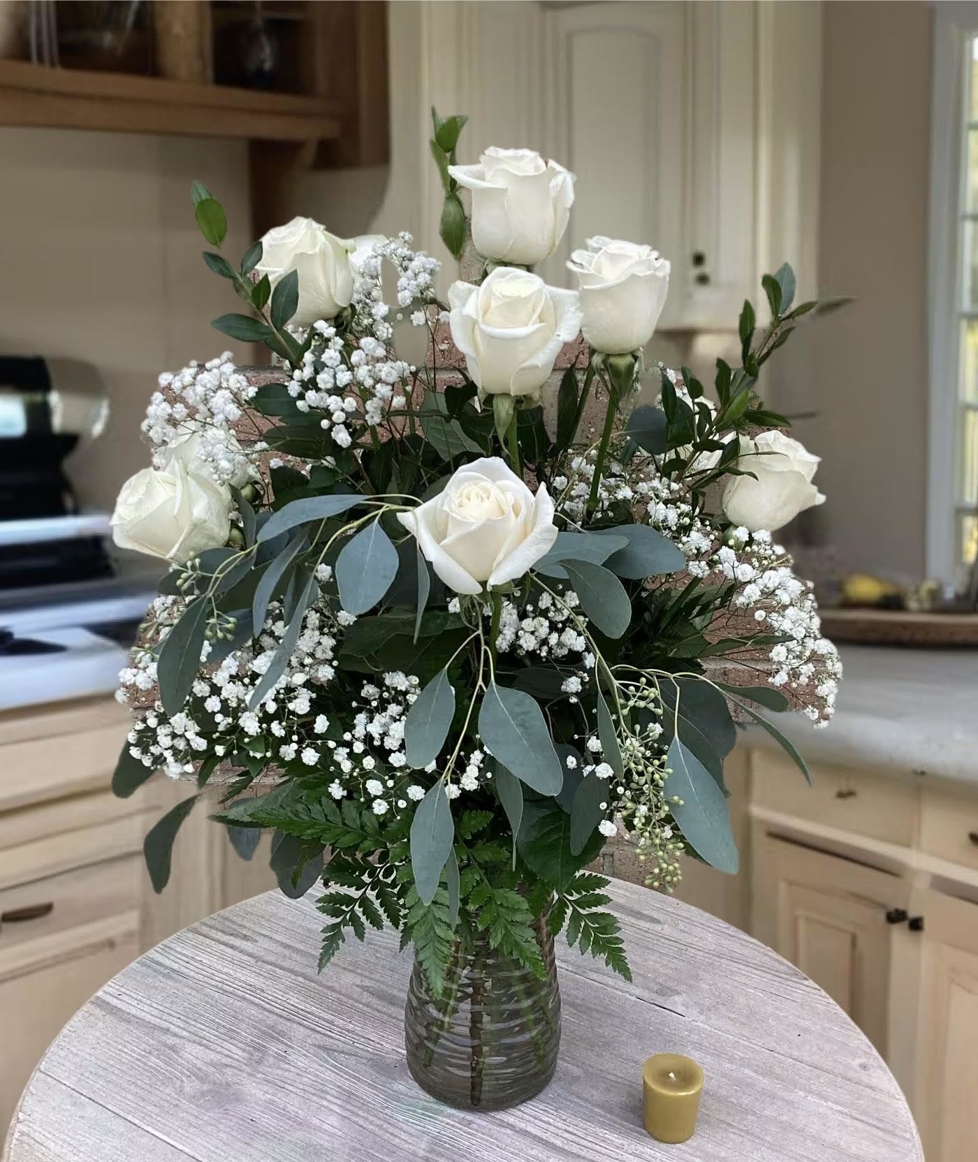White roses arranged in a glass vase with baby's breath and greenery
