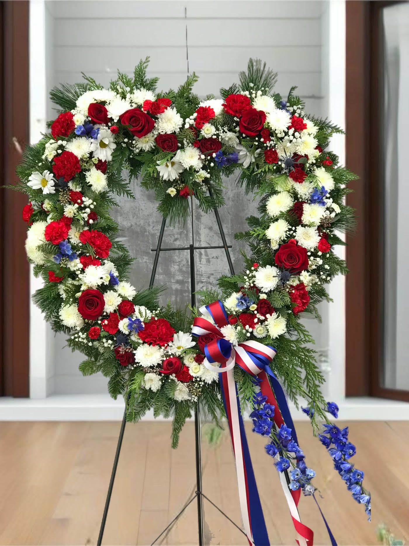 Heart-shaped floral wreath with red, white, and blue flowers on a stand