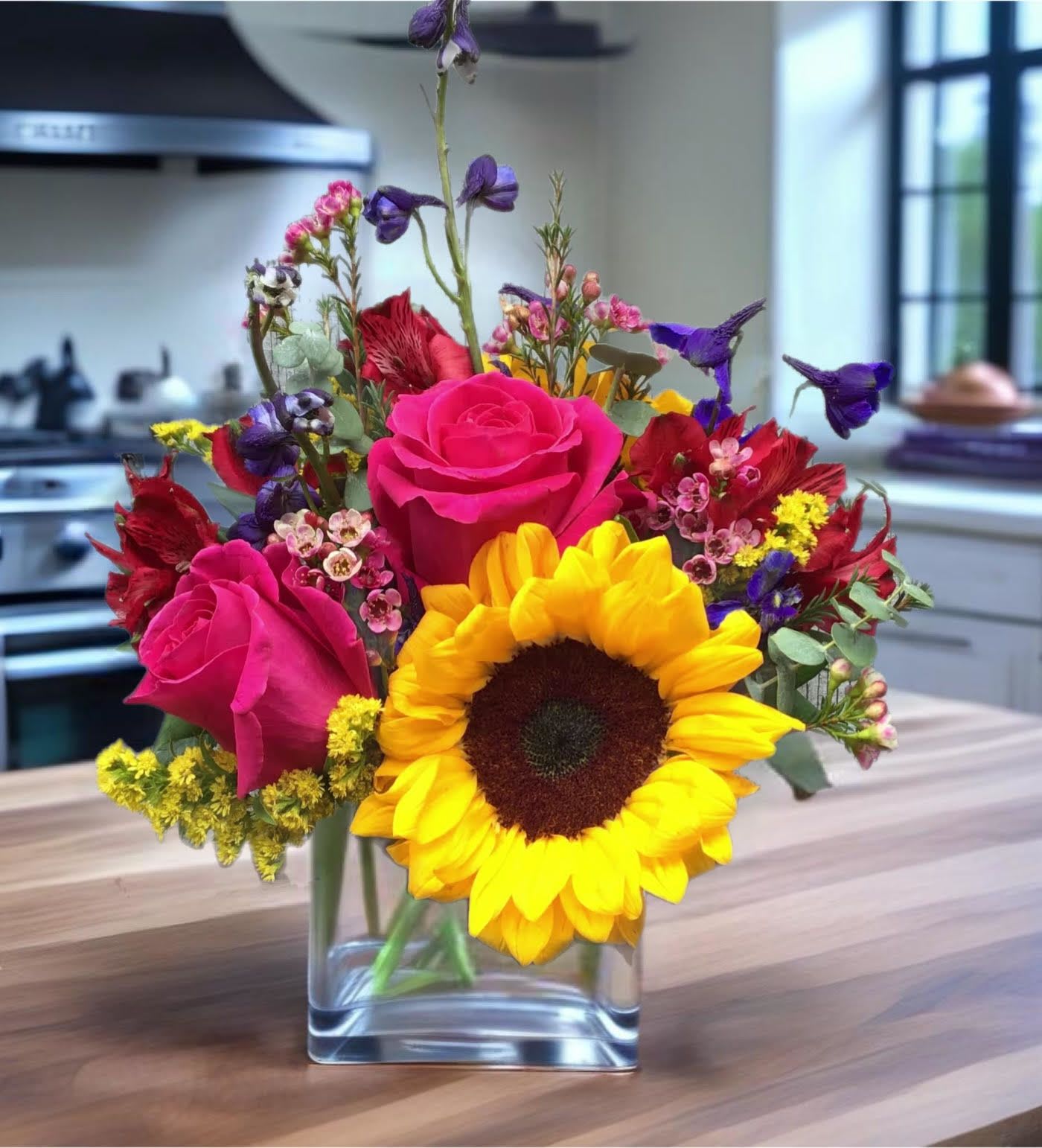 Bright mixed bouquet with sunflowers and pink roses in a clear glass vase