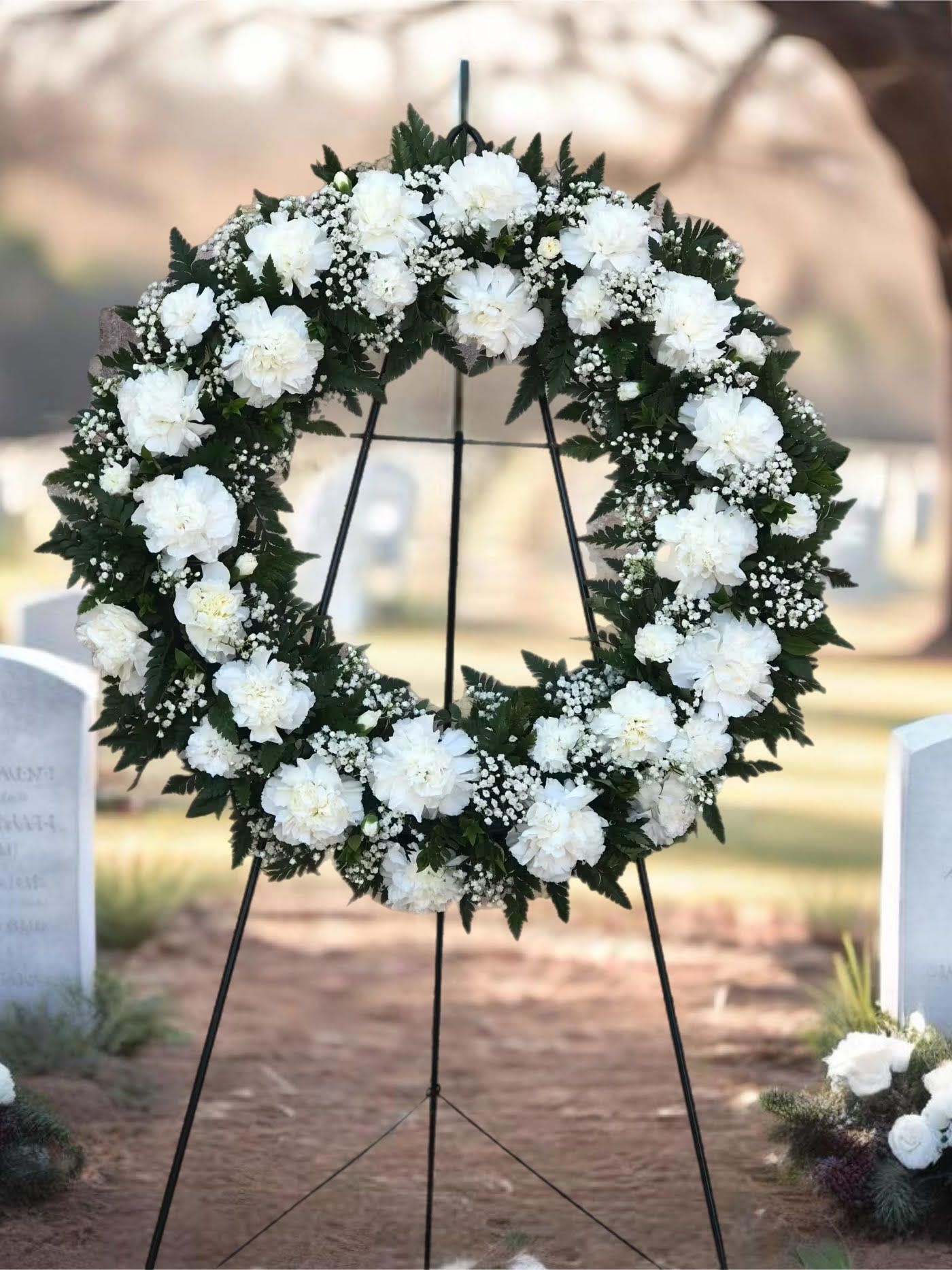 White floral wreath on a black stand at a gravesite