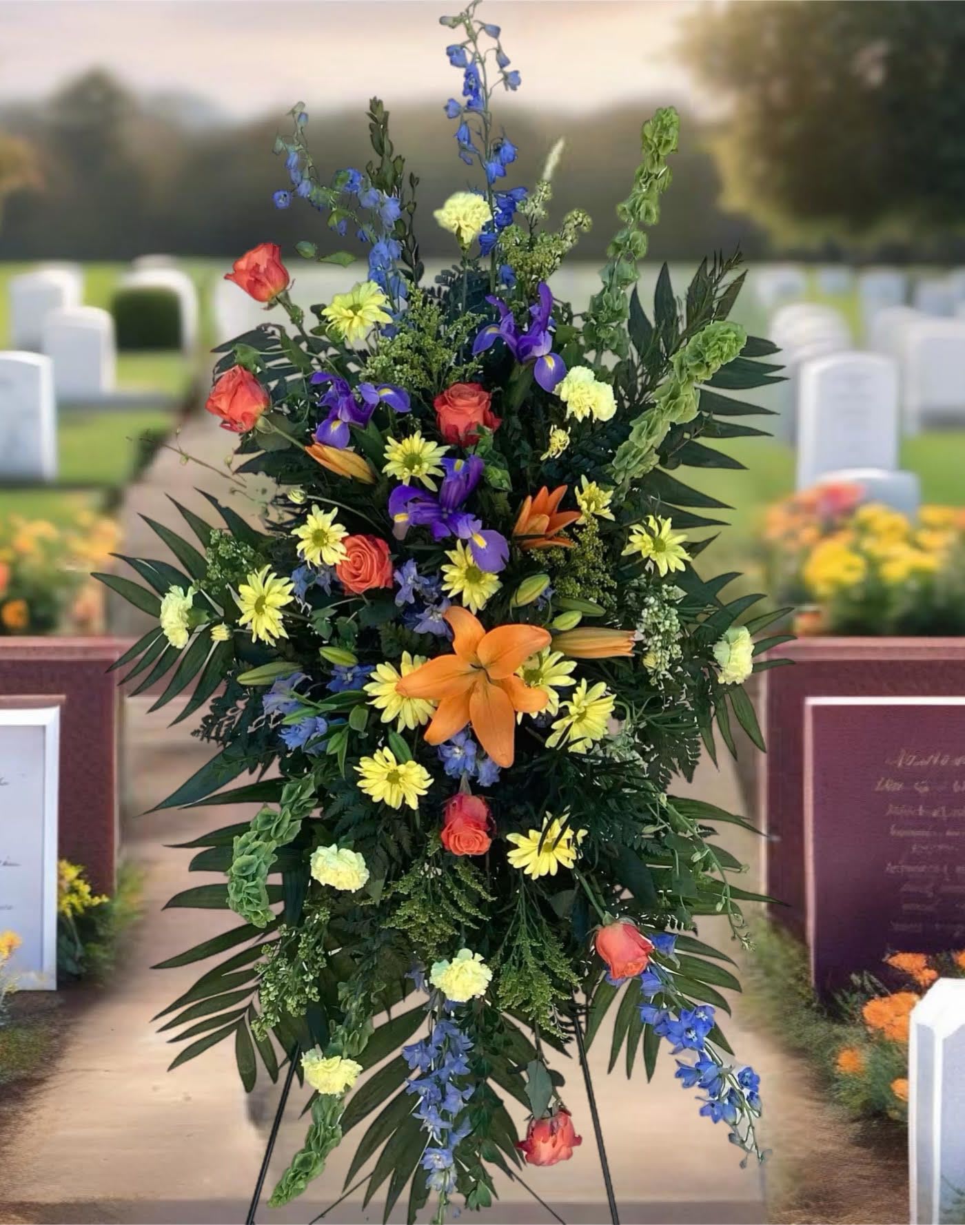 Tall funeral spray with orange, yellow, purple, and blue flowers