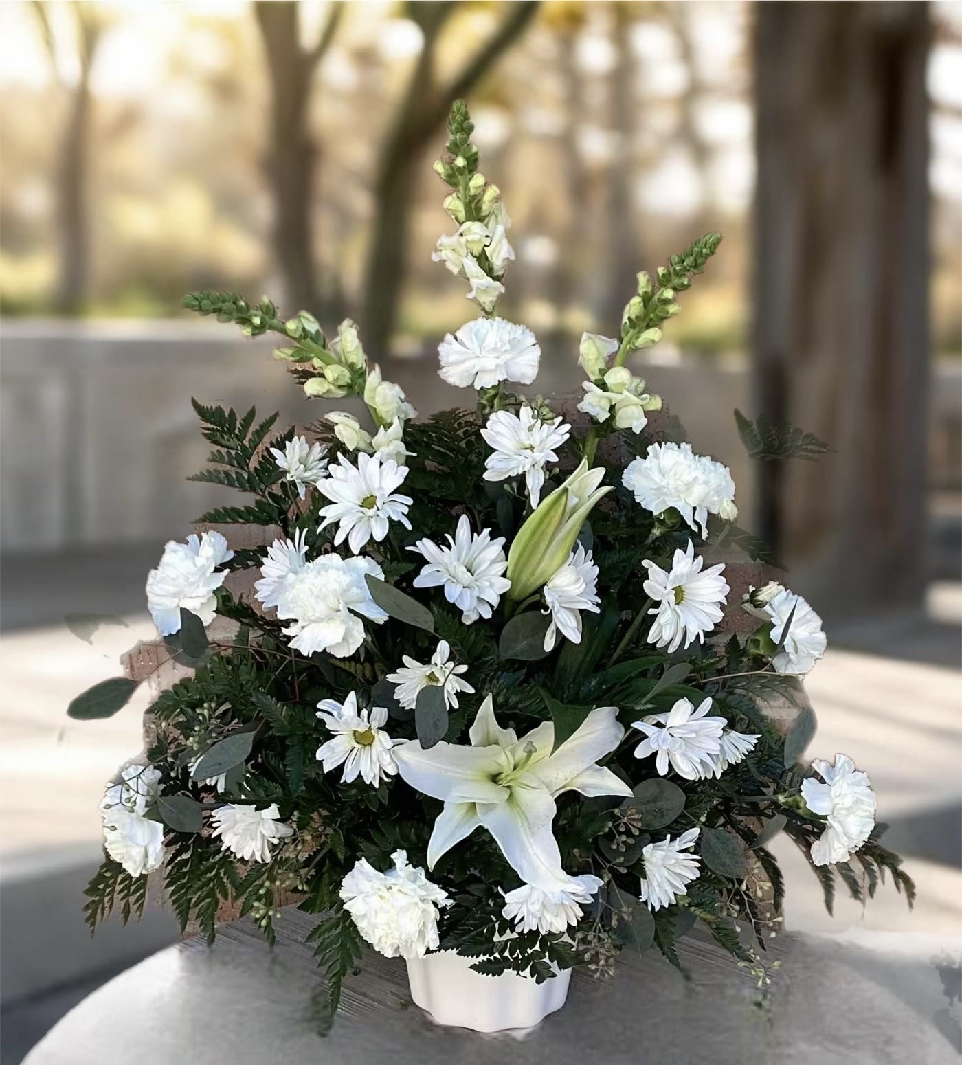 White flowers arranged in a low white vase with dark greenery.