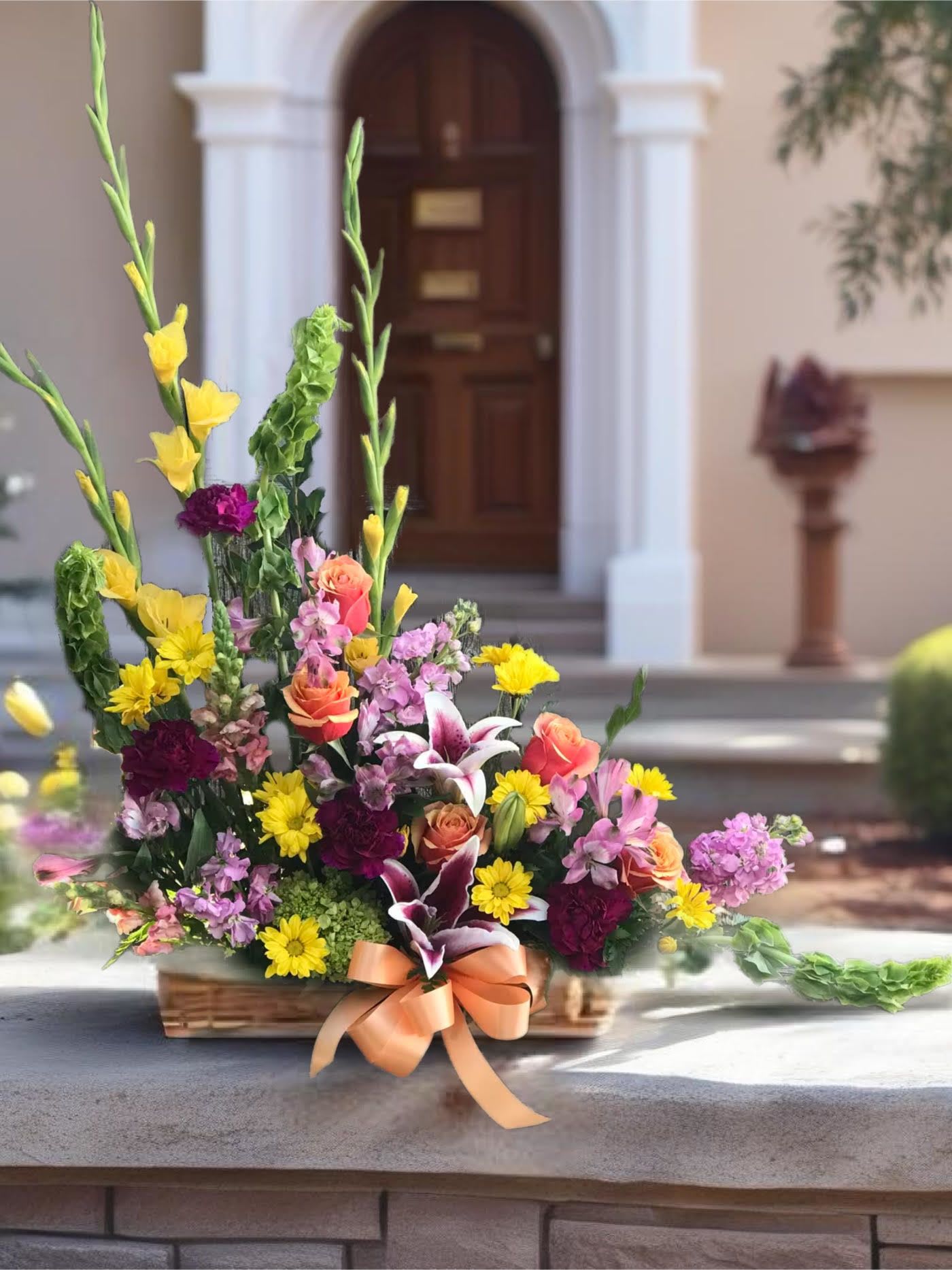 Colorful mixed flower arrangement in a basket with a peach ribbon