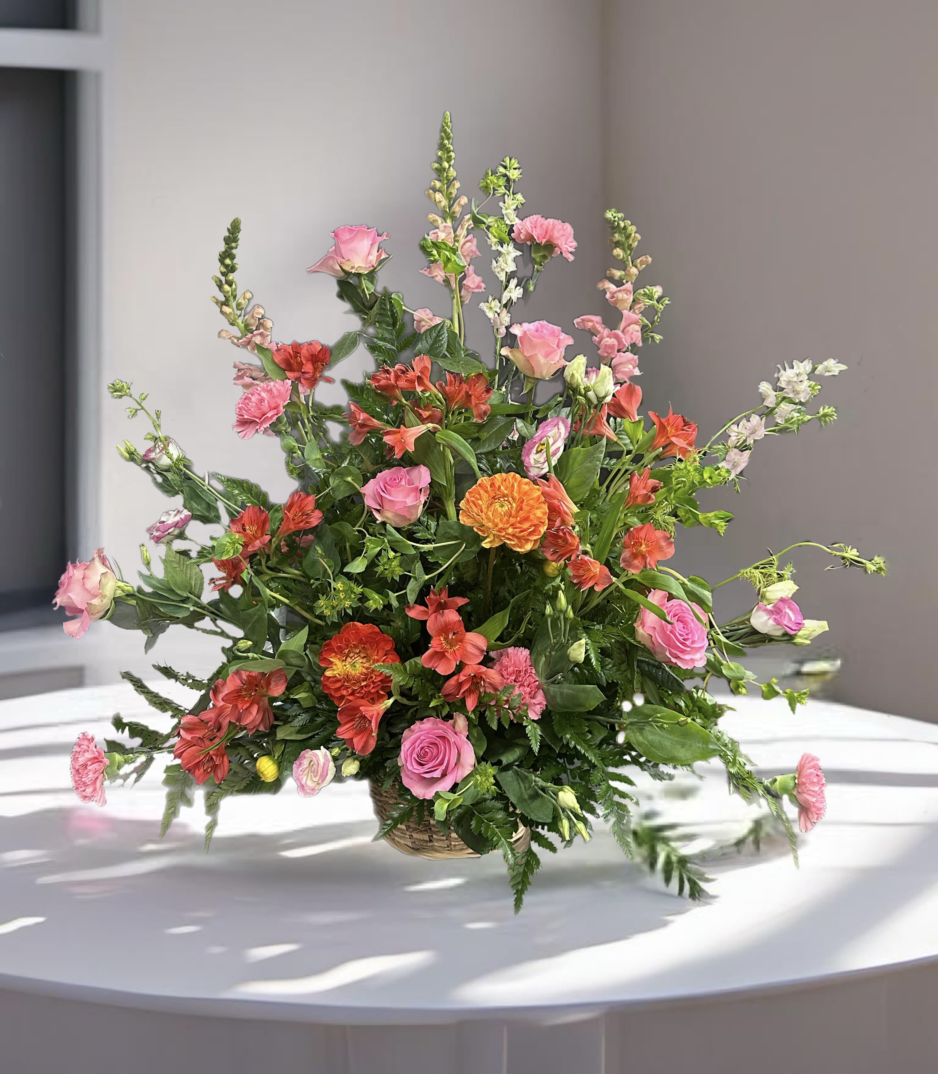 Mixed pink and orange flowers in a low basket arrangement