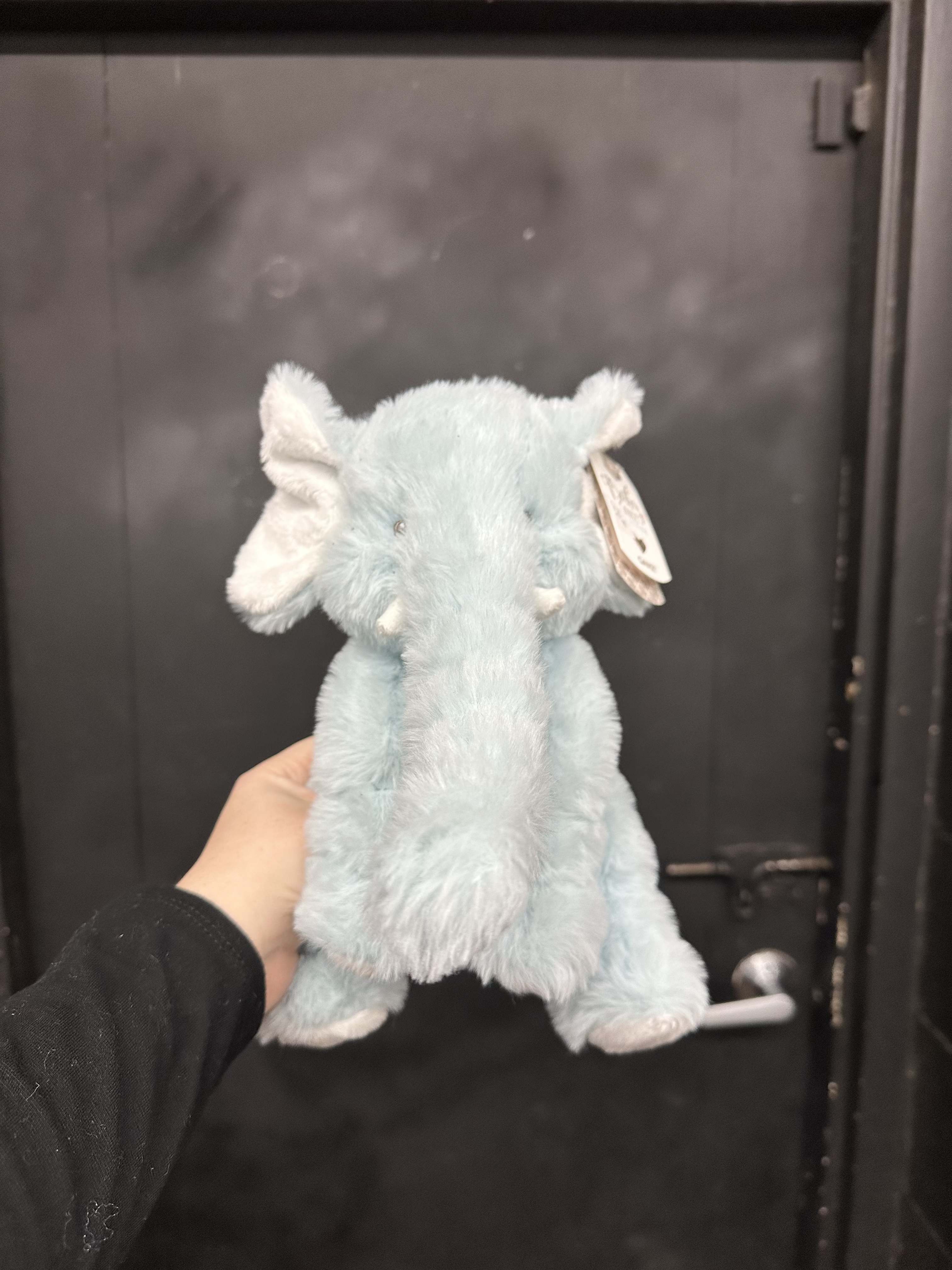 Light blue plush elephant toy being held in front of a dark door