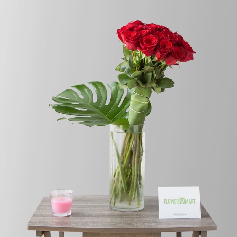 Red roses in a tall glass vase with a large tropical leaf