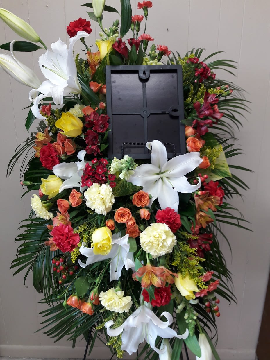 Standing funeral wreath with white lilies, roses, and carnations around a photo frame
