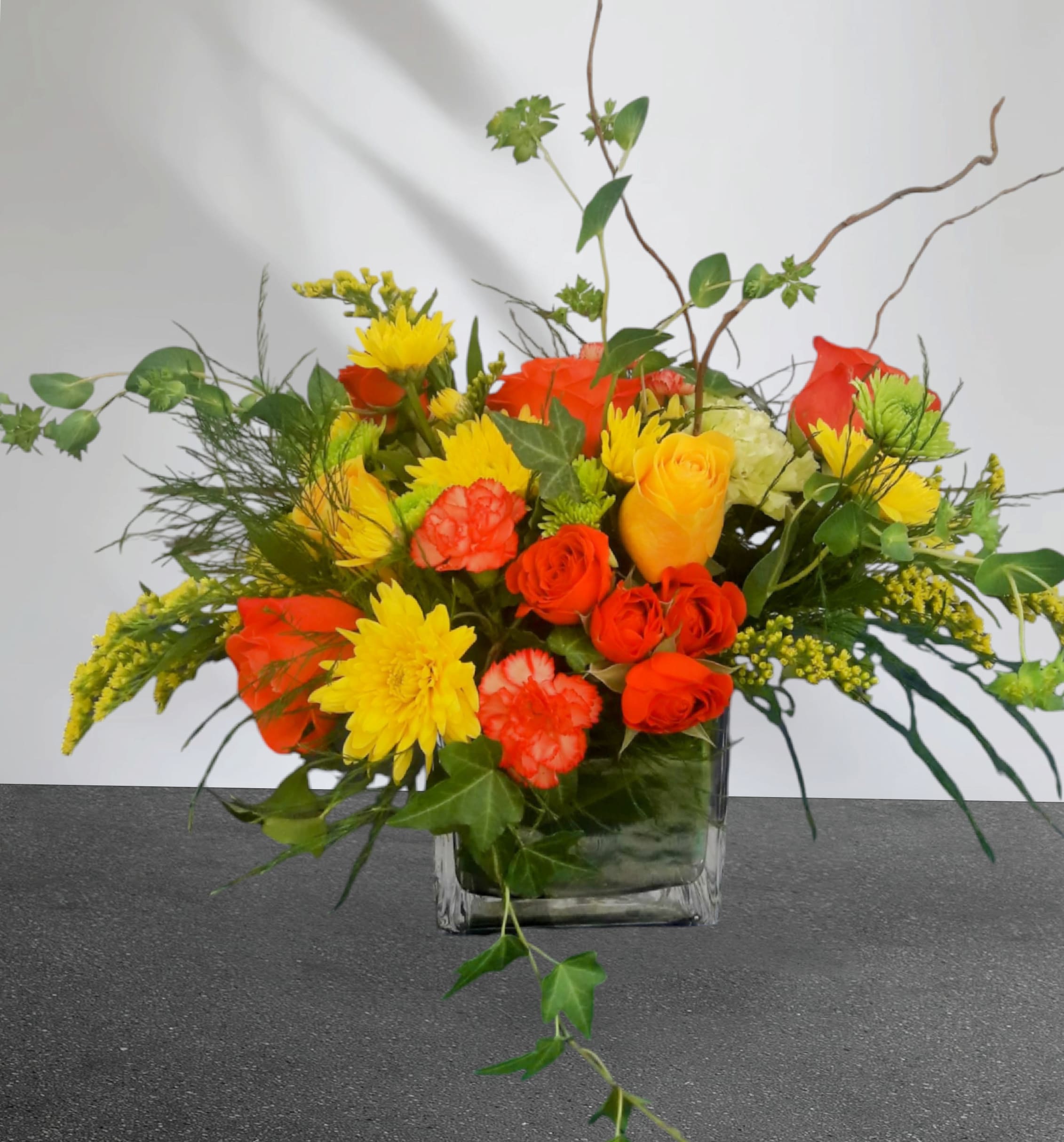 Mixed bouquet of yellow and orange flowers in a square glass vase