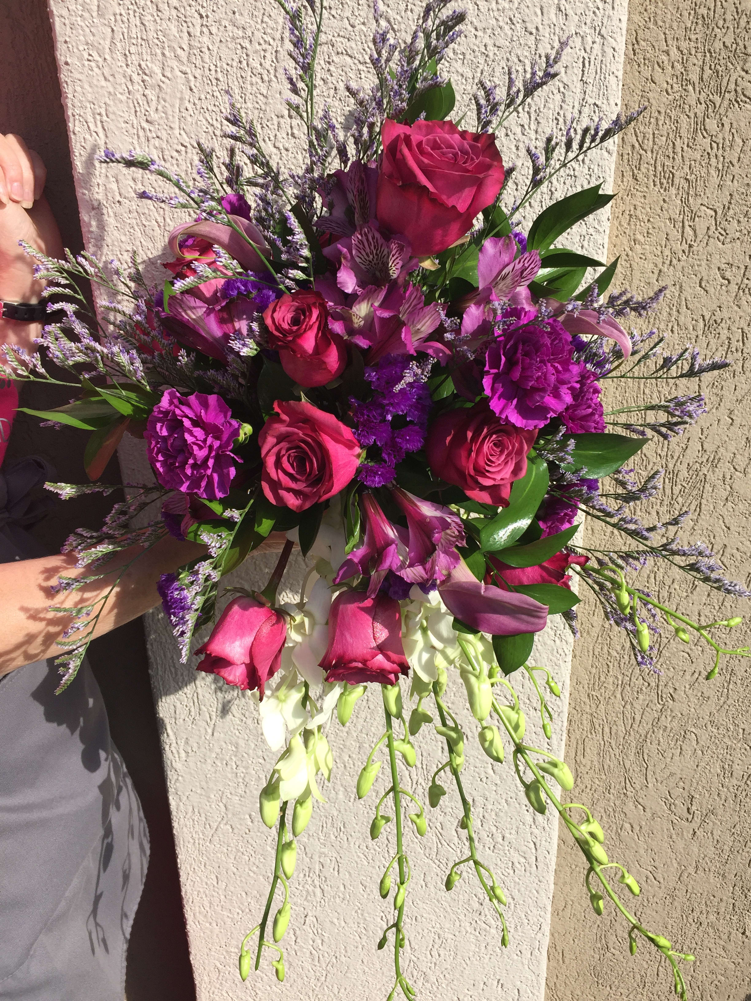 Handheld bouquet of pink roses and purple flowers with trailing white blooms