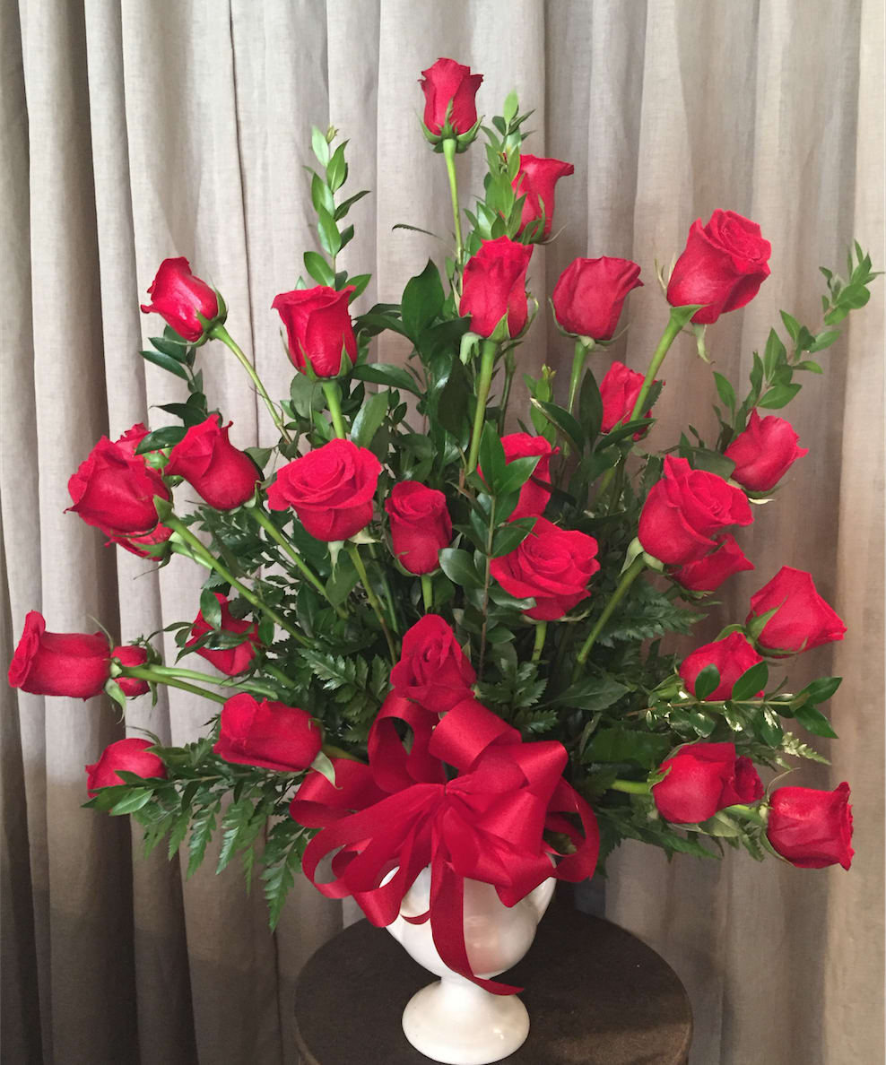 Red roses arranged in a white vase with a red ribbon bow