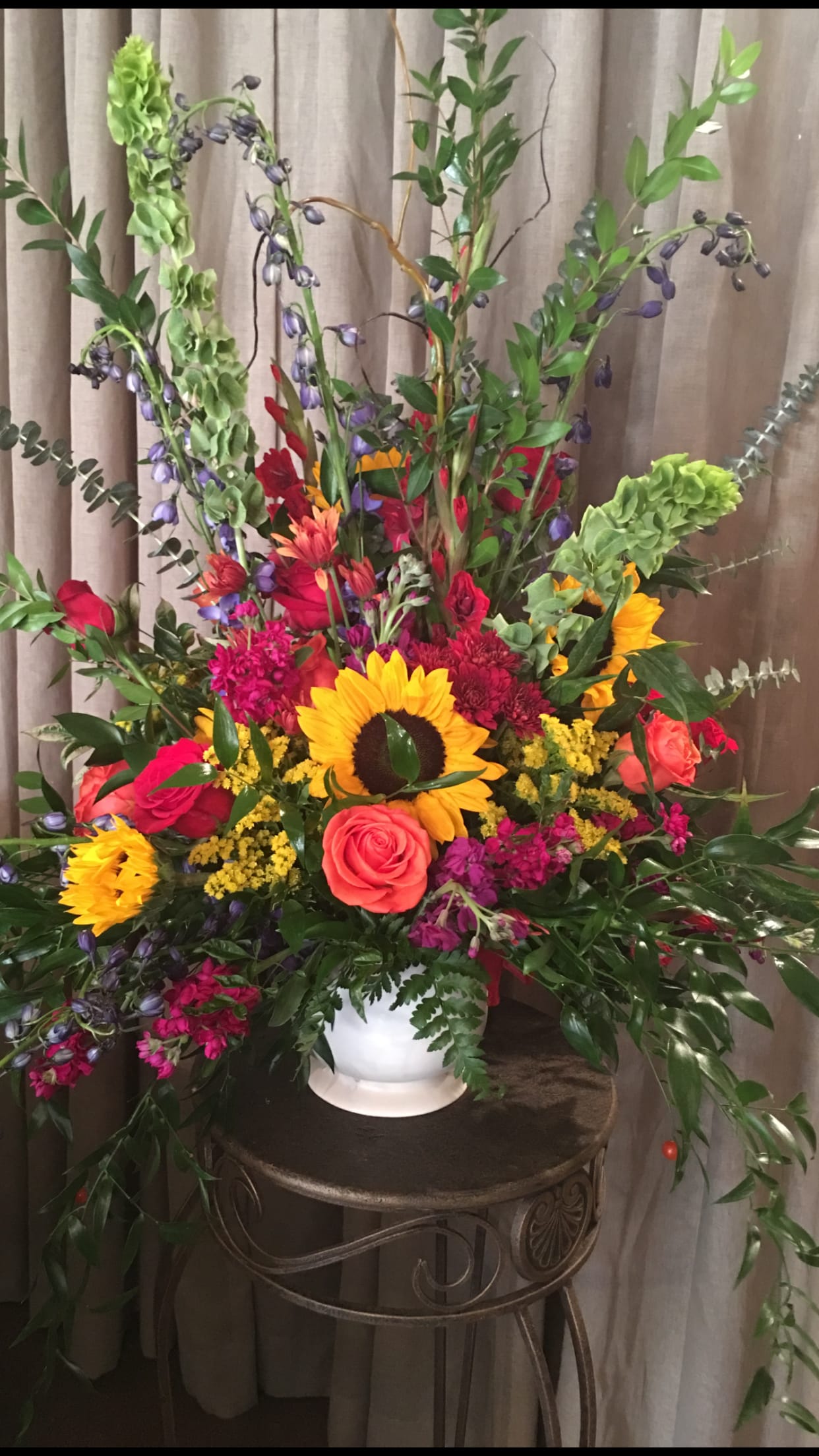 Tall mixed flower arrangement in a white vase with sunflowers and roses