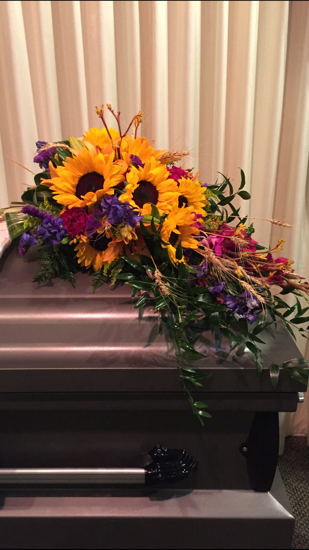 Sunflower arrangement with purple and pink flowers on a casket