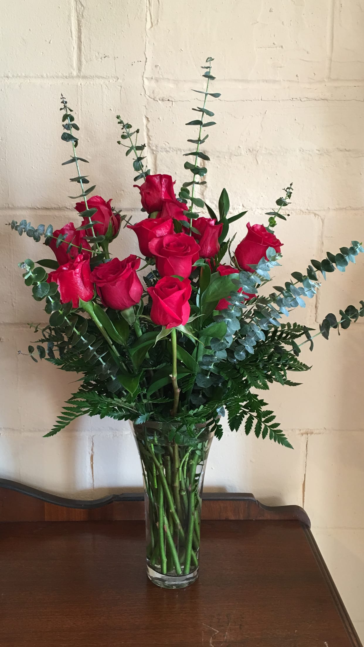 Red roses in a clear glass vase with tall eucalyptus stems