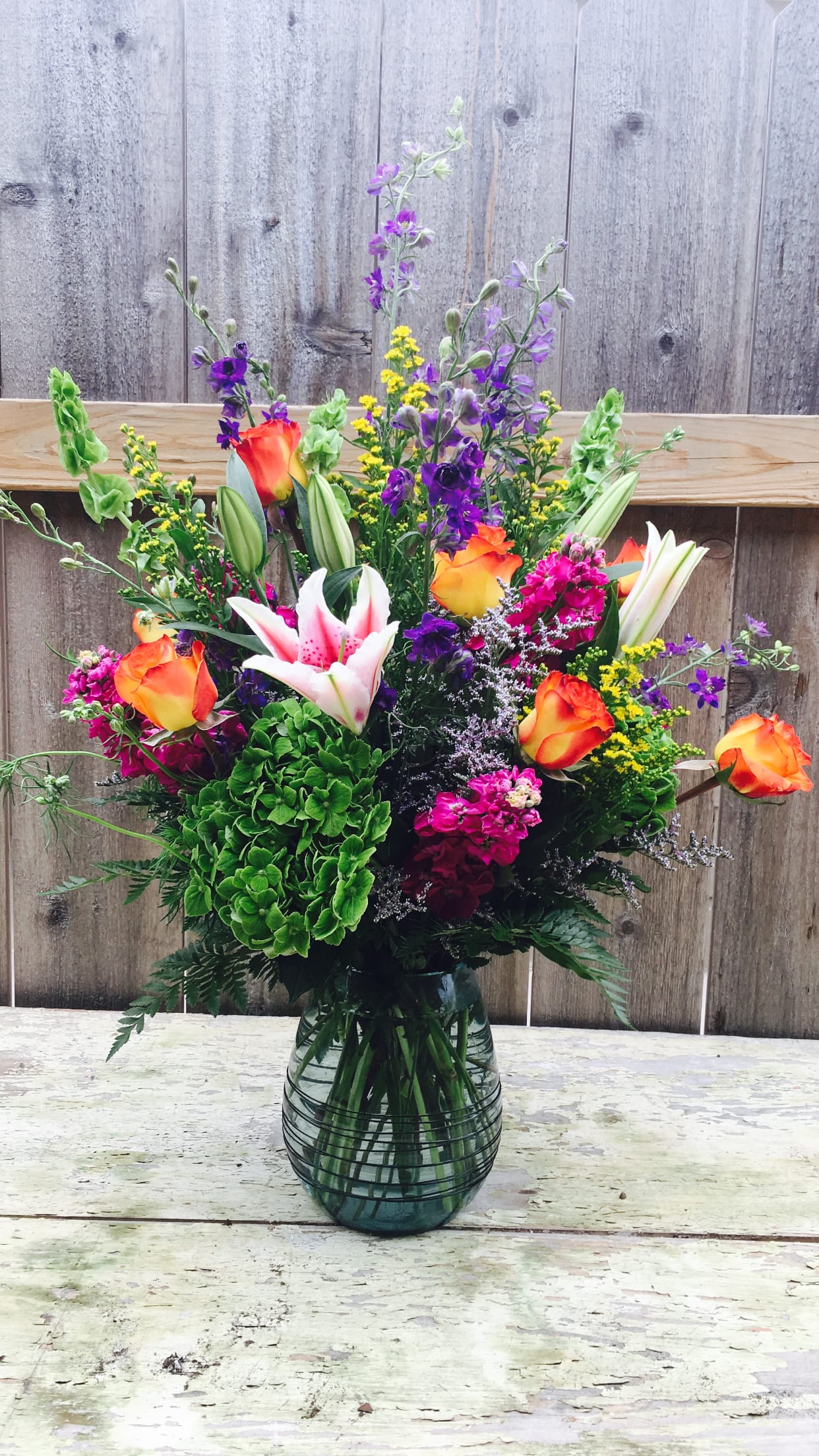 Colorful mixed bouquet in a glass vase with roses, lilies, and purple flowers