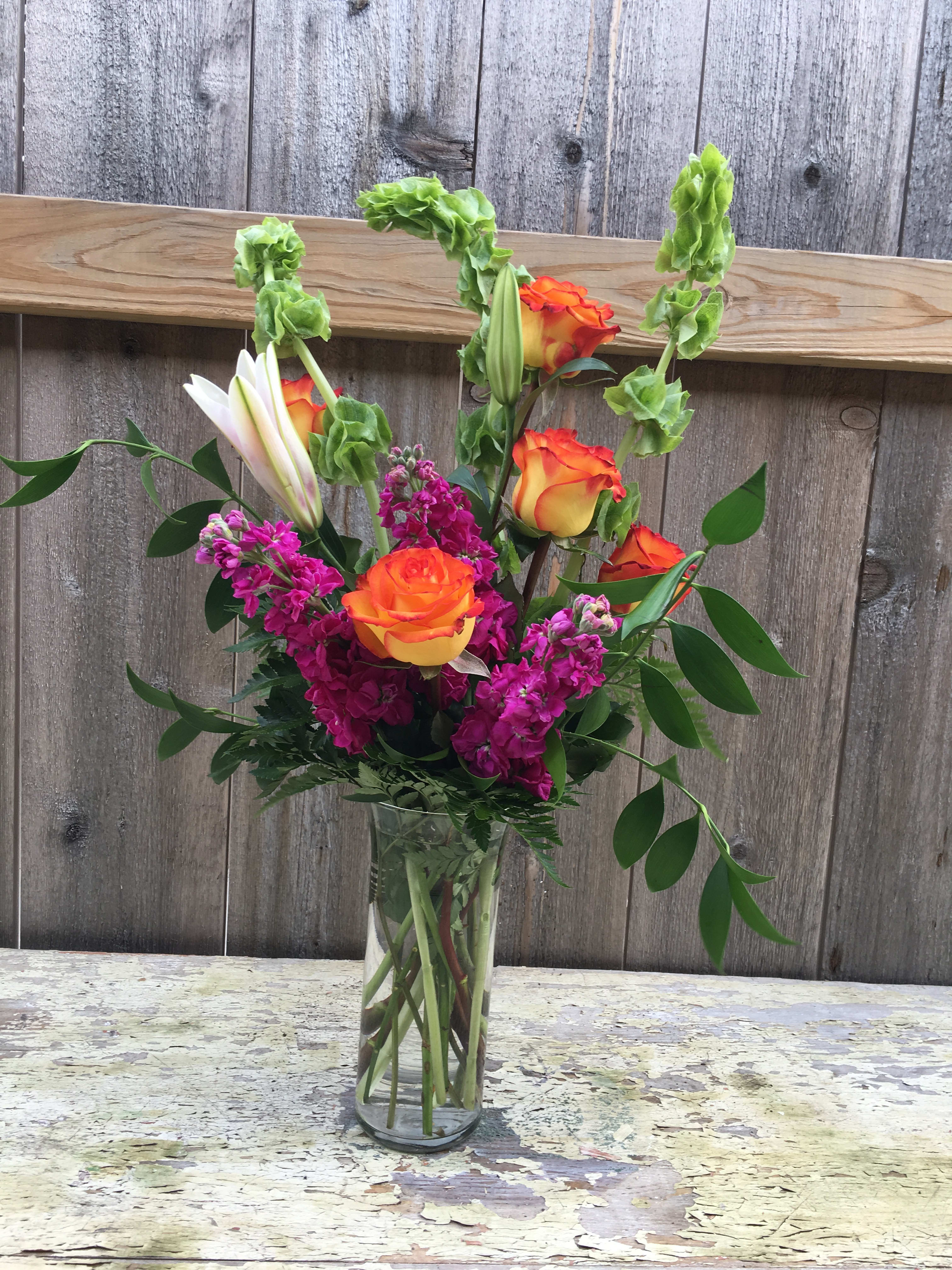 Orange and yellow roses in a clear glass vase with magenta flowers