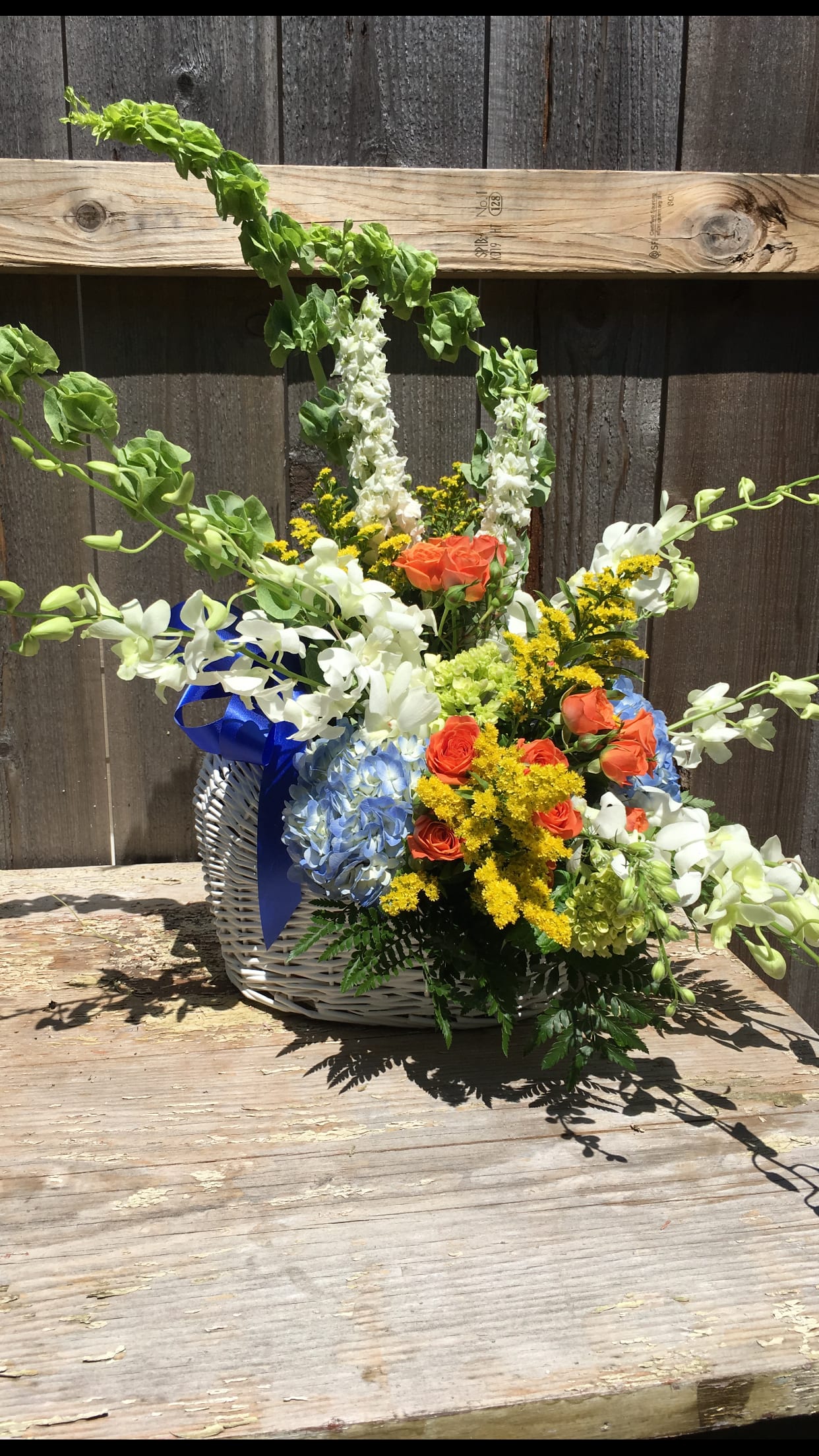 Mixed flower basket with white orchids, orange roses, blue hydrangea, and yellow filler