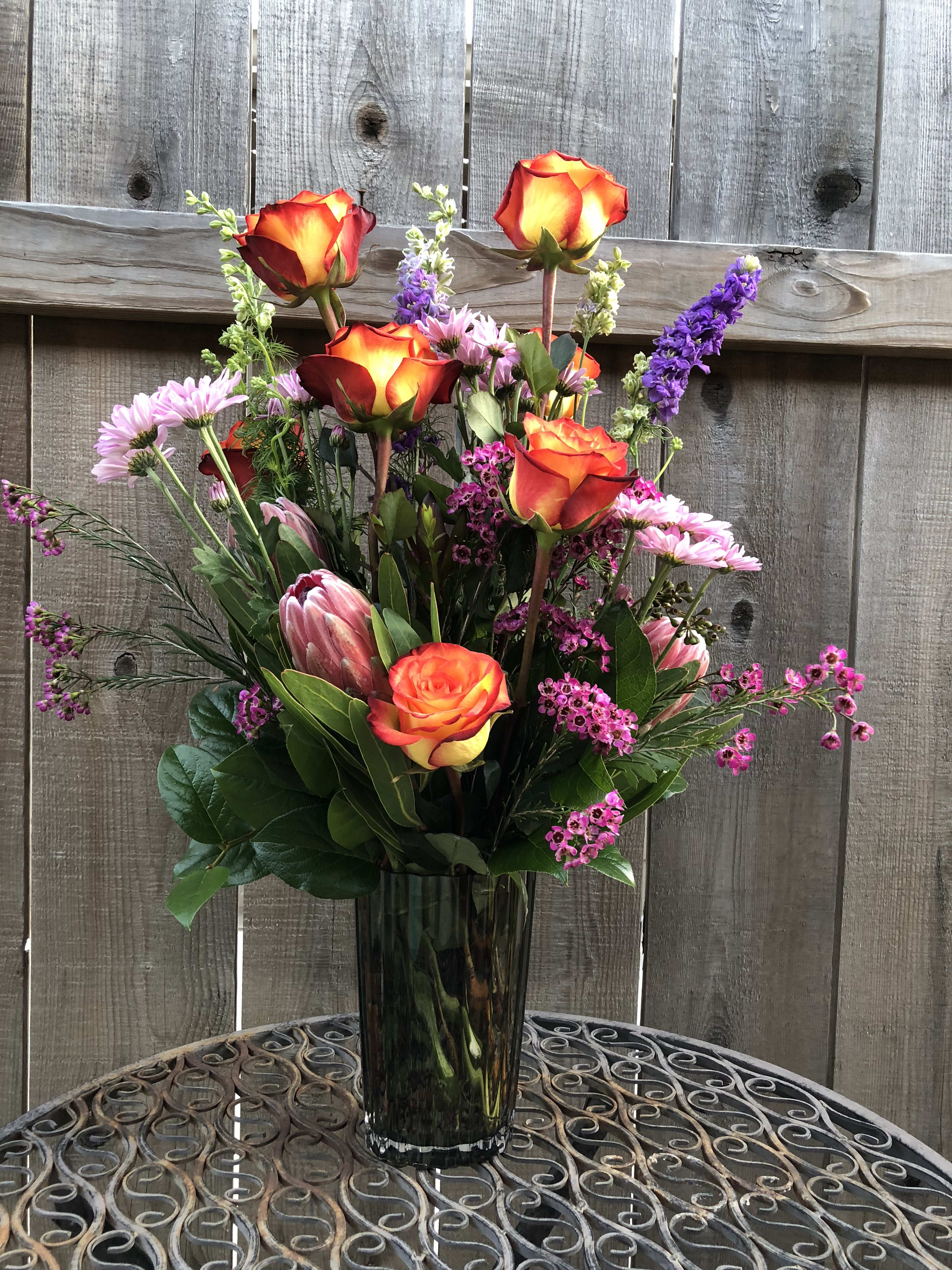 Tall bouquet of orange-red roses and pink flowers in a glass vase