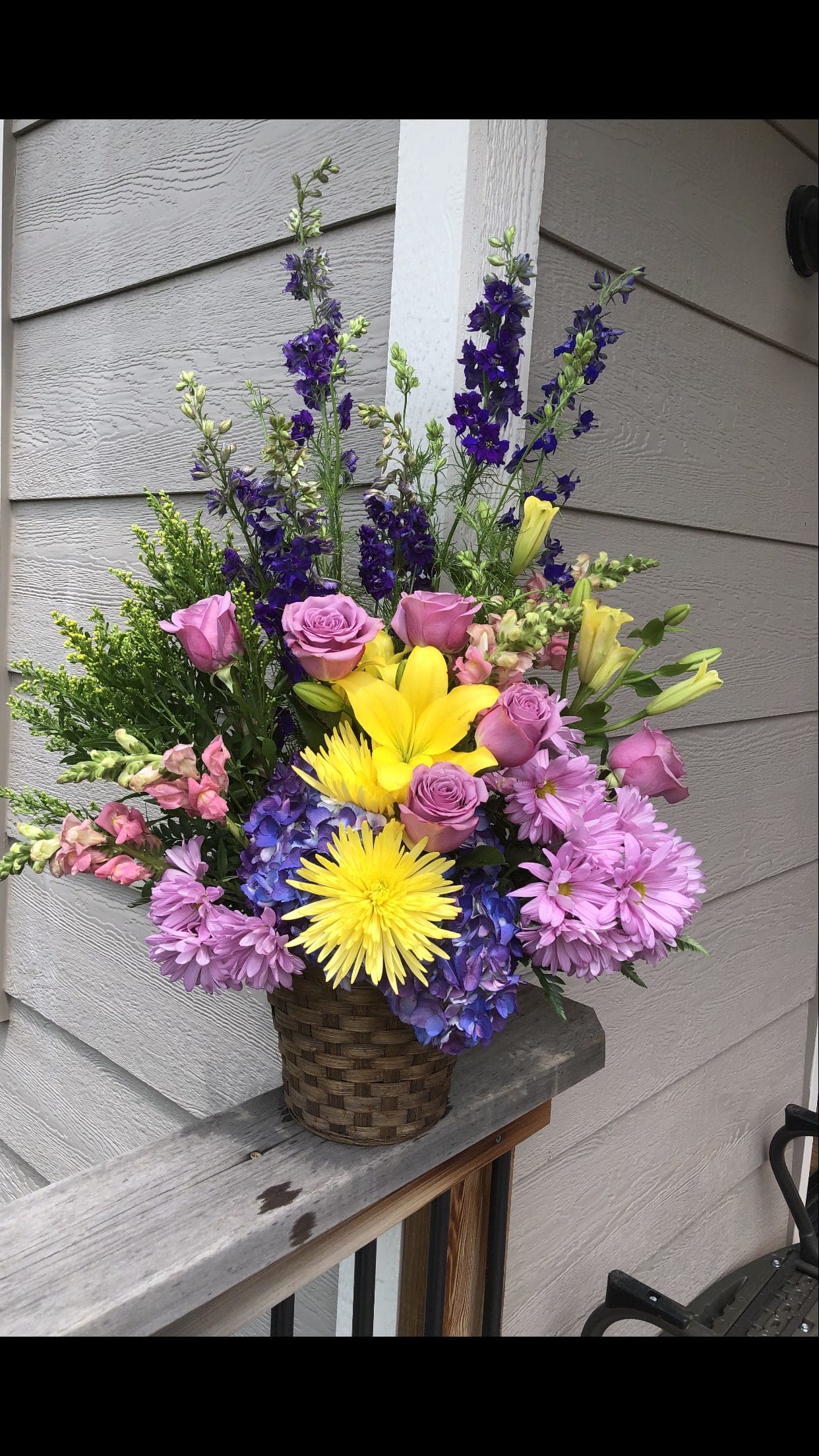 Mixed bouquet in a woven basket with pink, yellow, purple, and blue flowers