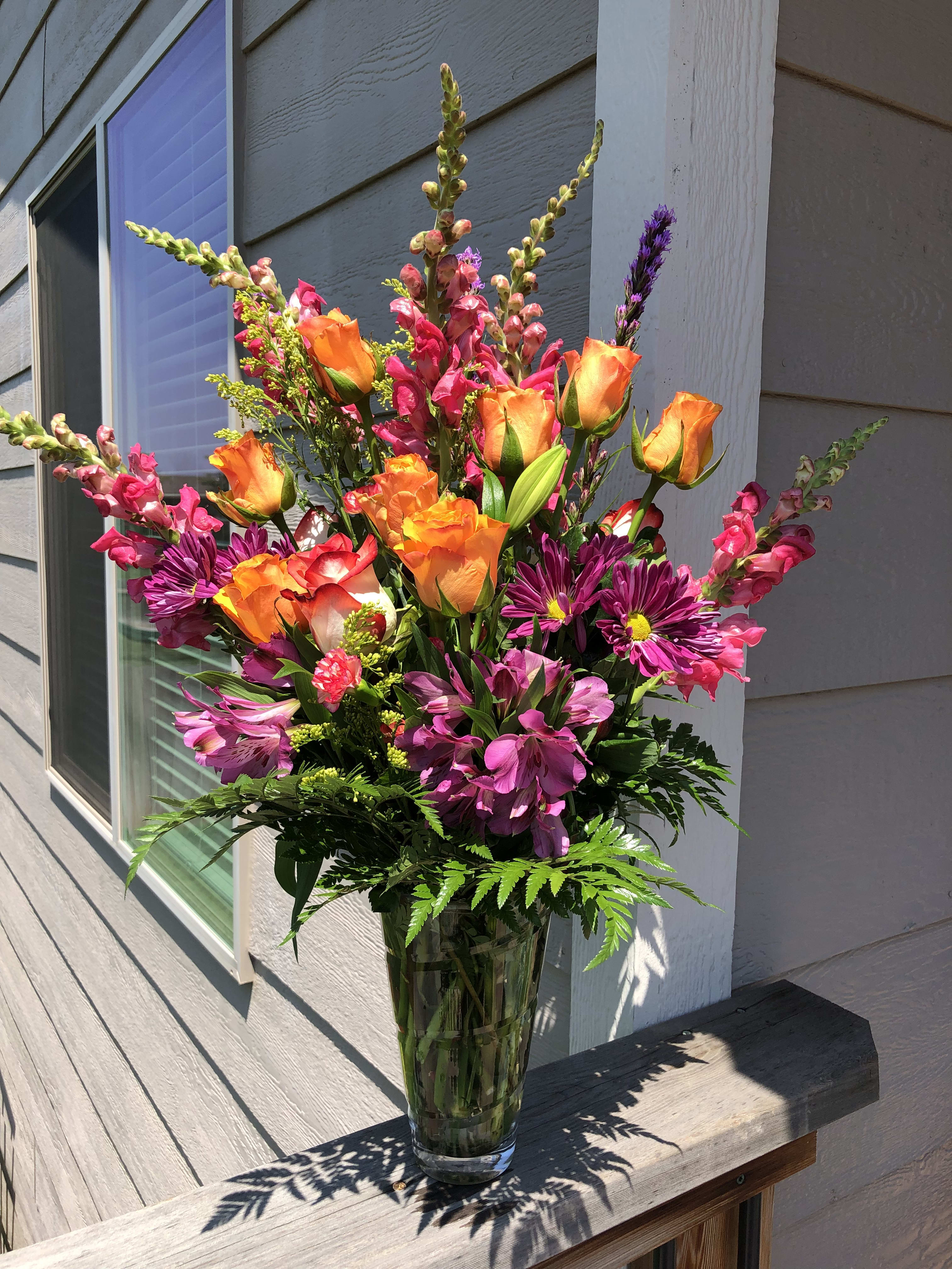 Tall bouquet of orange roses, pink snapdragons, and purple daisies in a glass vase