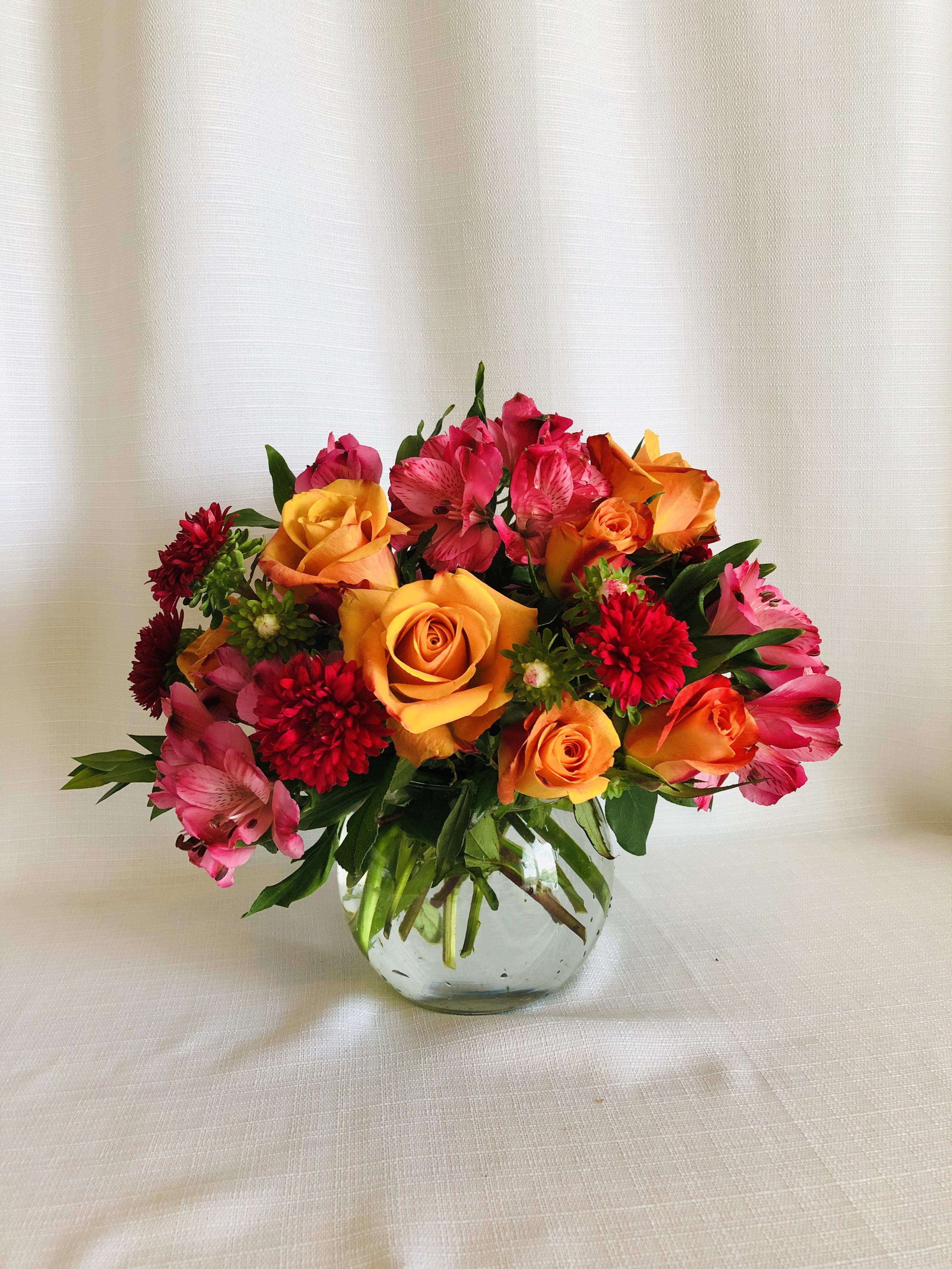 Mixed bouquet of orange roses, pink alstroemeria, and red blooms in a glass vase