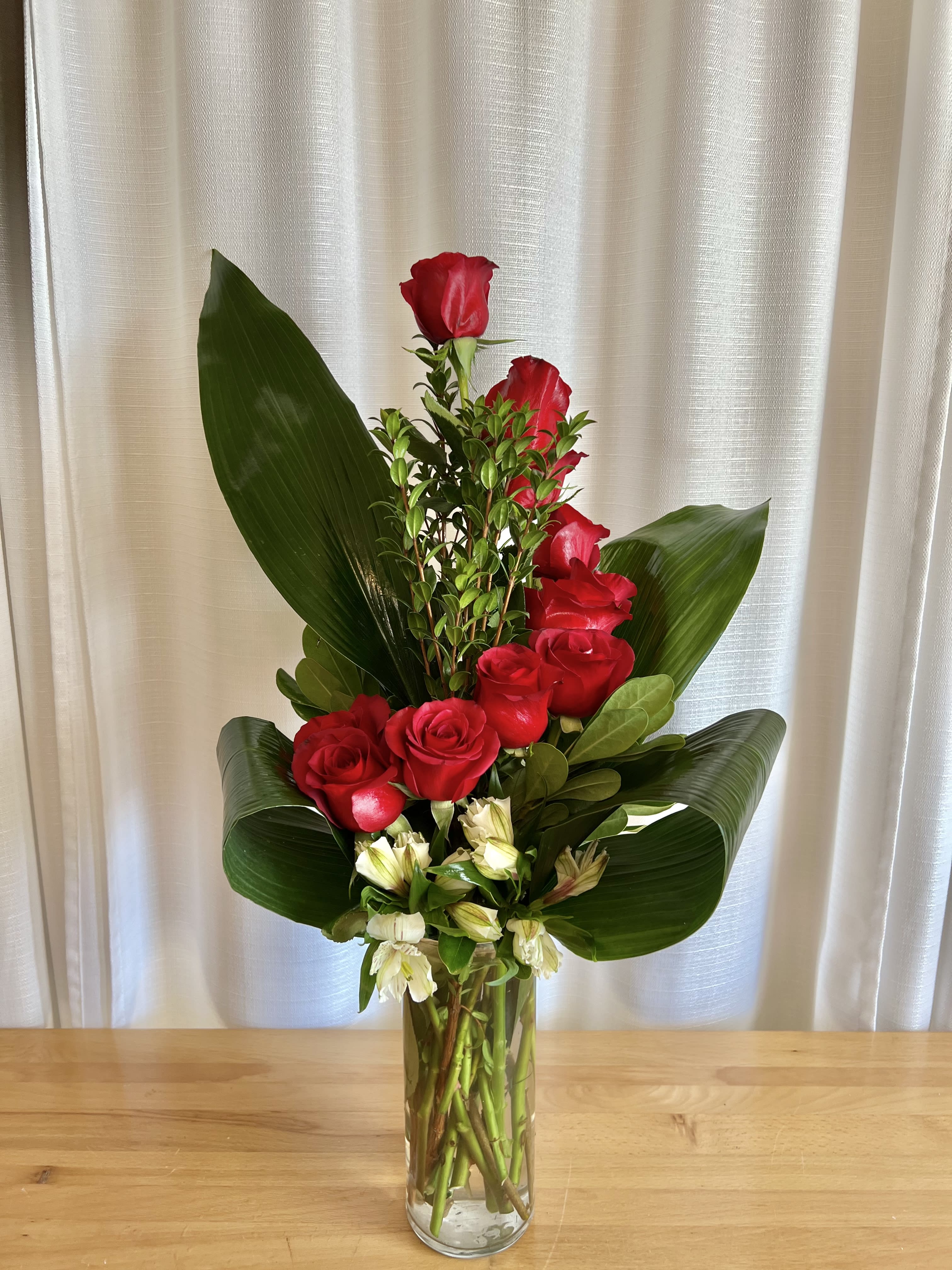 Tall red rose arrangement in a clear glass vase with broad green leaves