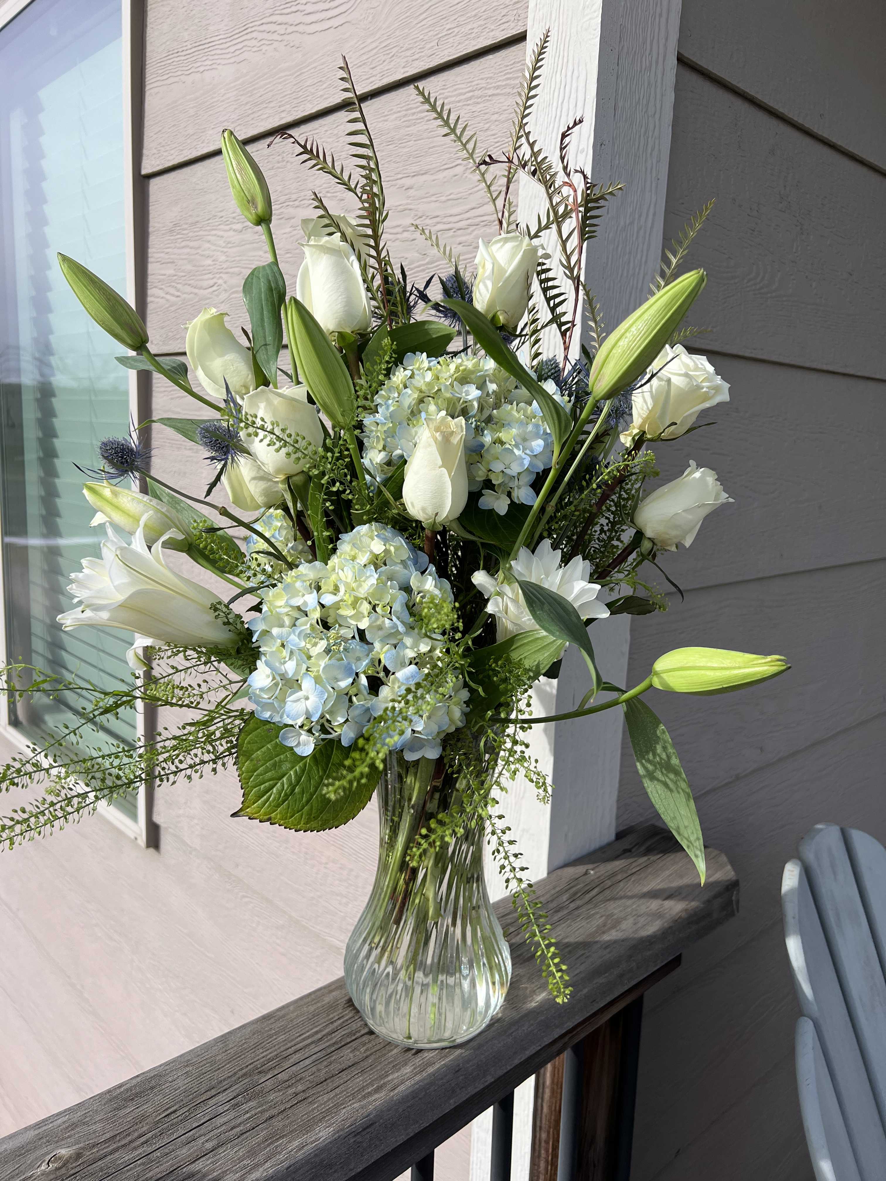 White roses and lilies arranged with blue hydrangeas in a glass vase