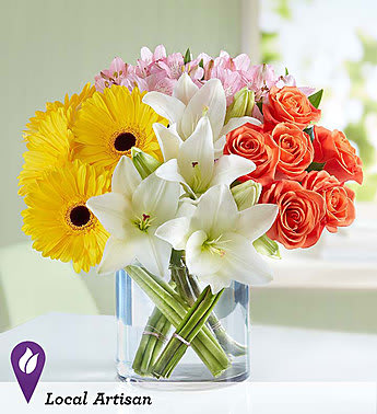 Bouquet of yellow gerbera daisies, white lilies, and orange roses in a glass vase