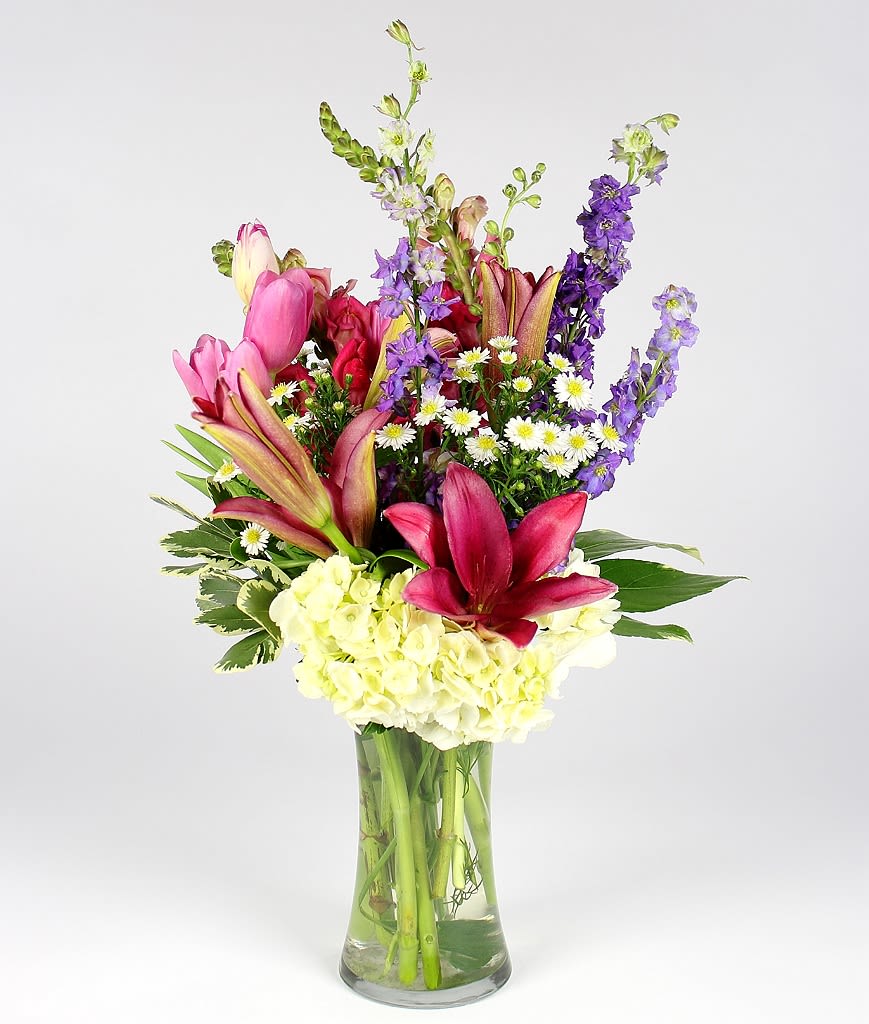 Colorful bouquet of lilies, hydrangea, and purple spikes in a glass vase