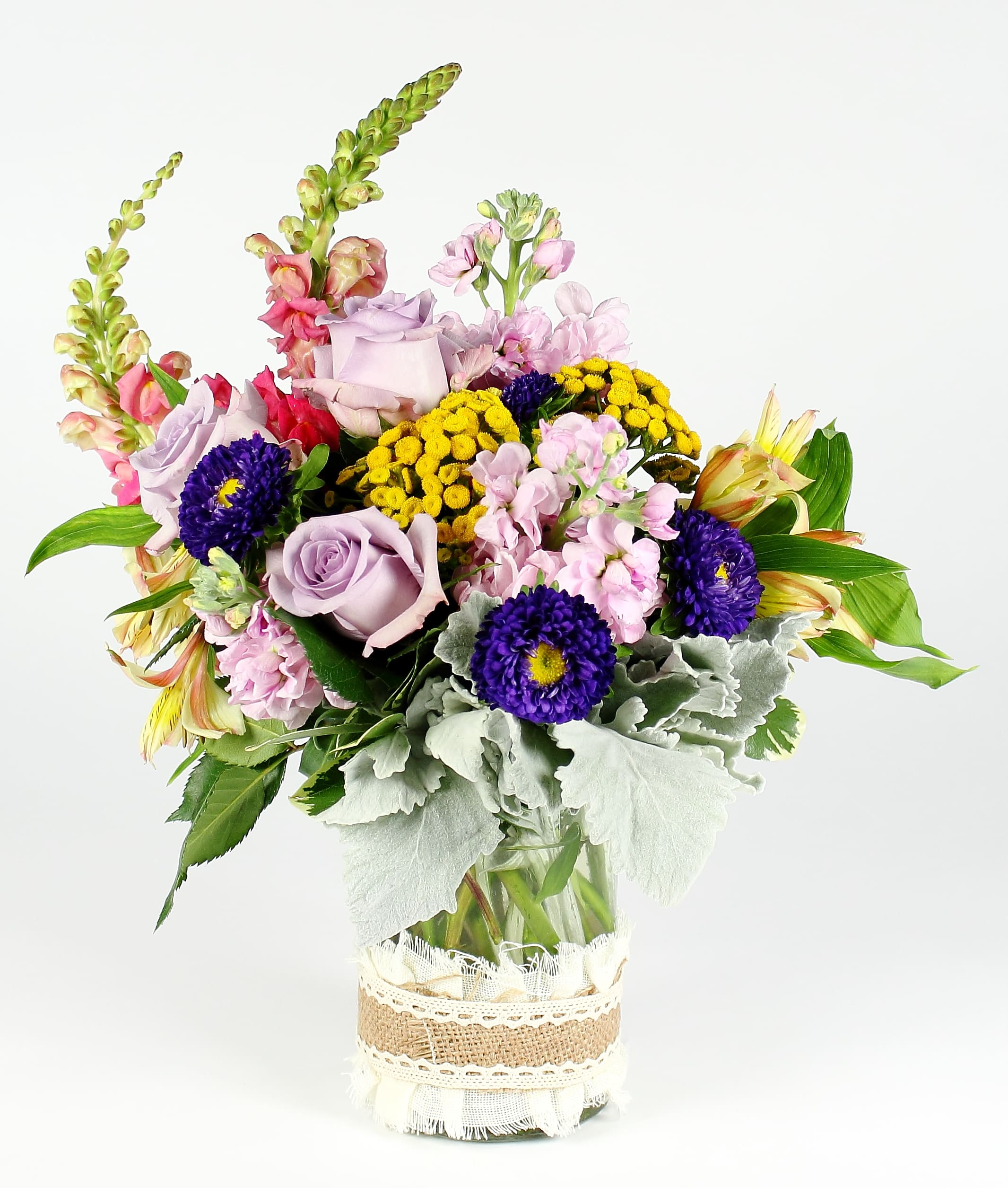 Mixed bouquet of lavender roses, pink blooms, and yellow flowers in a glass vase