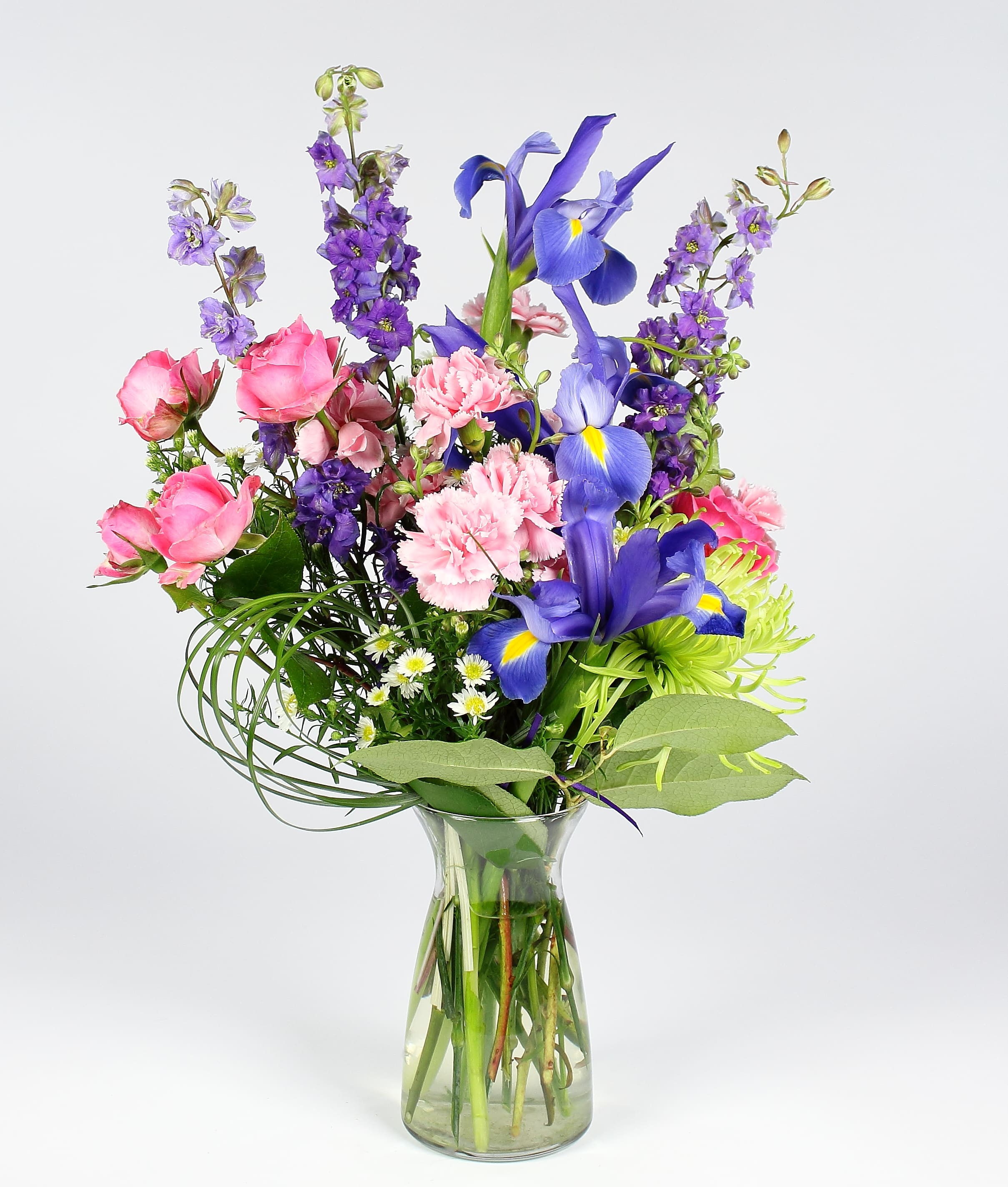 Mixed bouquet of pink, purple, and blue flowers in a clear glass vase