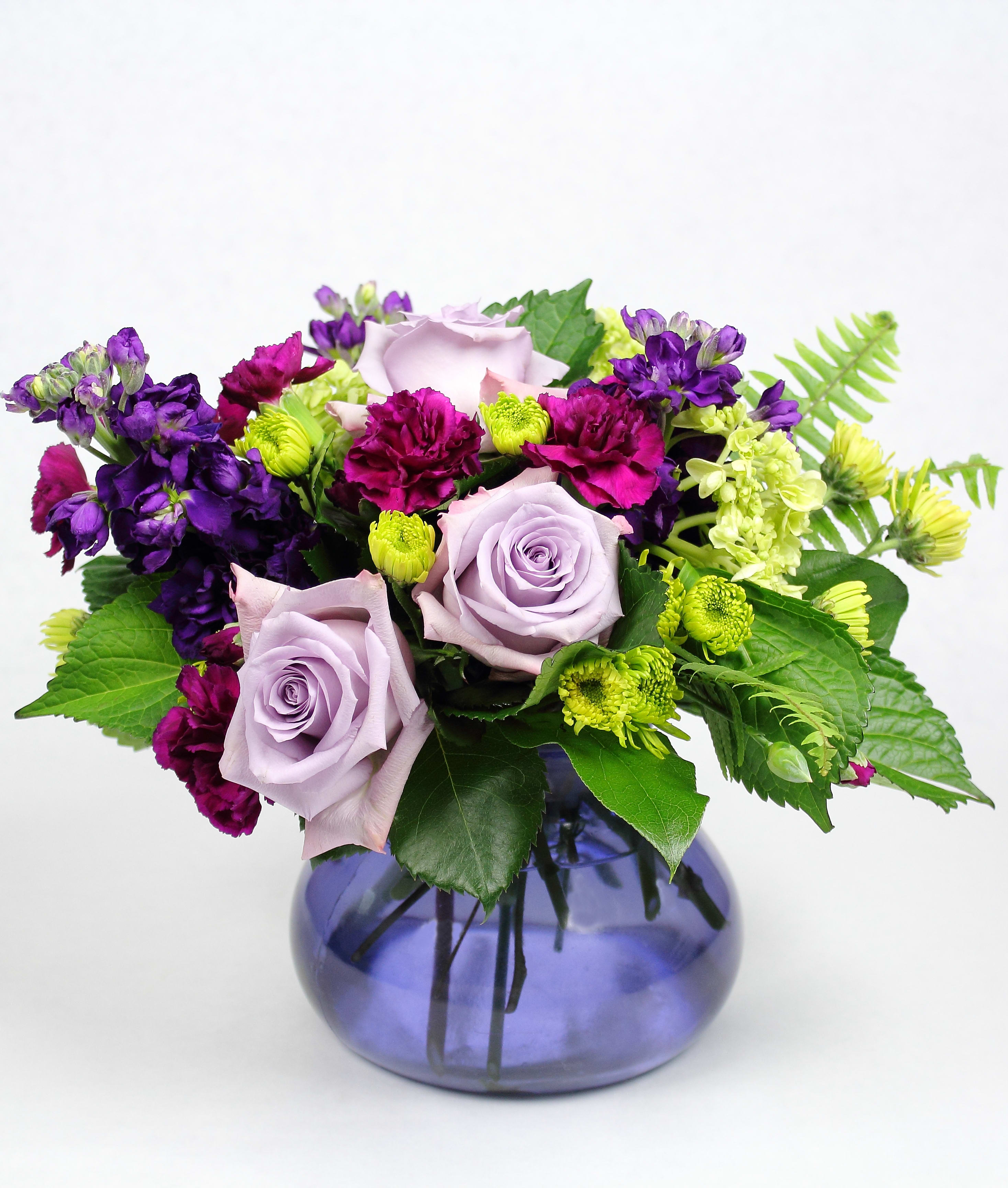 Lavender roses with purple and magenta flowers in a blue glass vase
