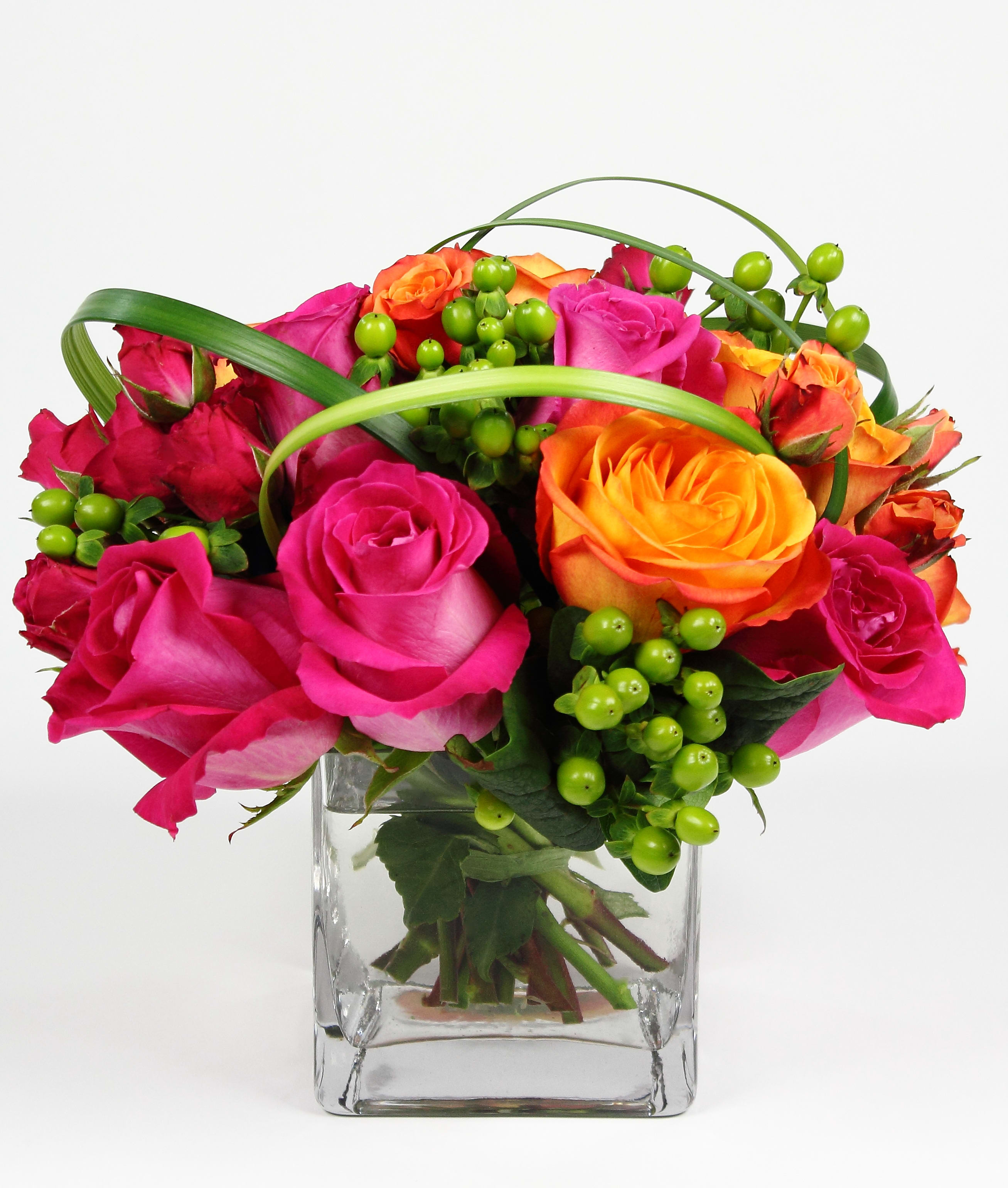 Pink and orange roses in a clear square vase with green berries